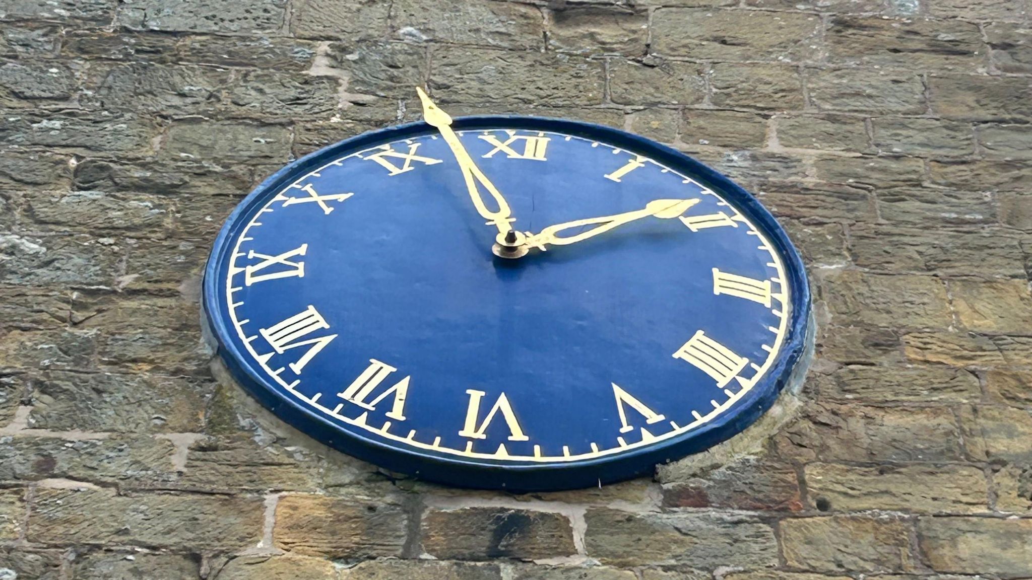 Close-up of a blue clock on a church. The time shows that it is a few minutes to two o'clock. The roman numeral for 11 is incorrect, with the numeral for nine in its place.