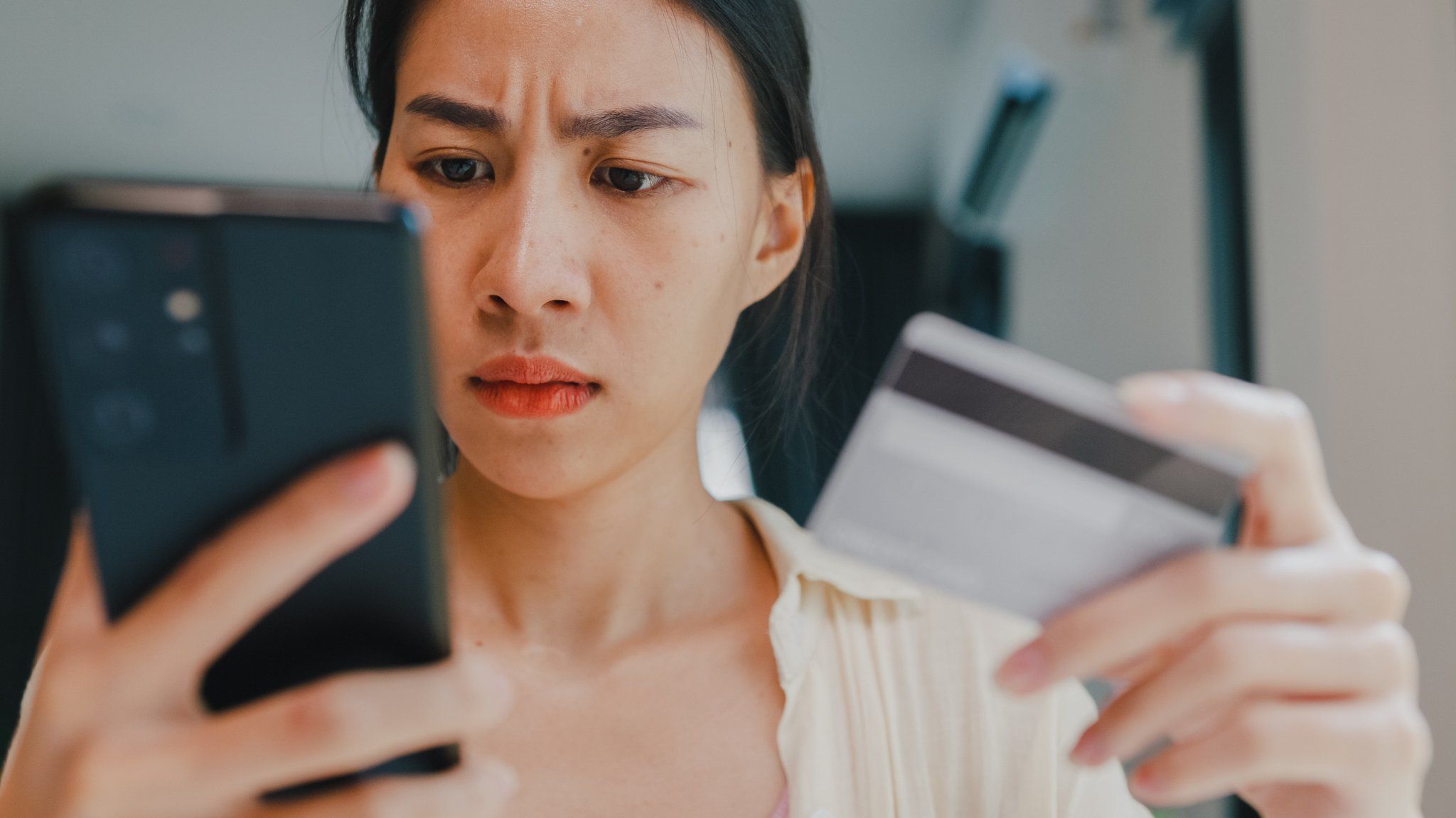 Woman looking worried holding phone and bank card