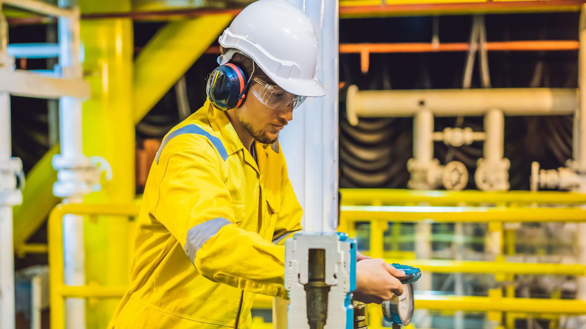 A man wearing a hard hat, ear defenders and yellow overalls working on an oil rig