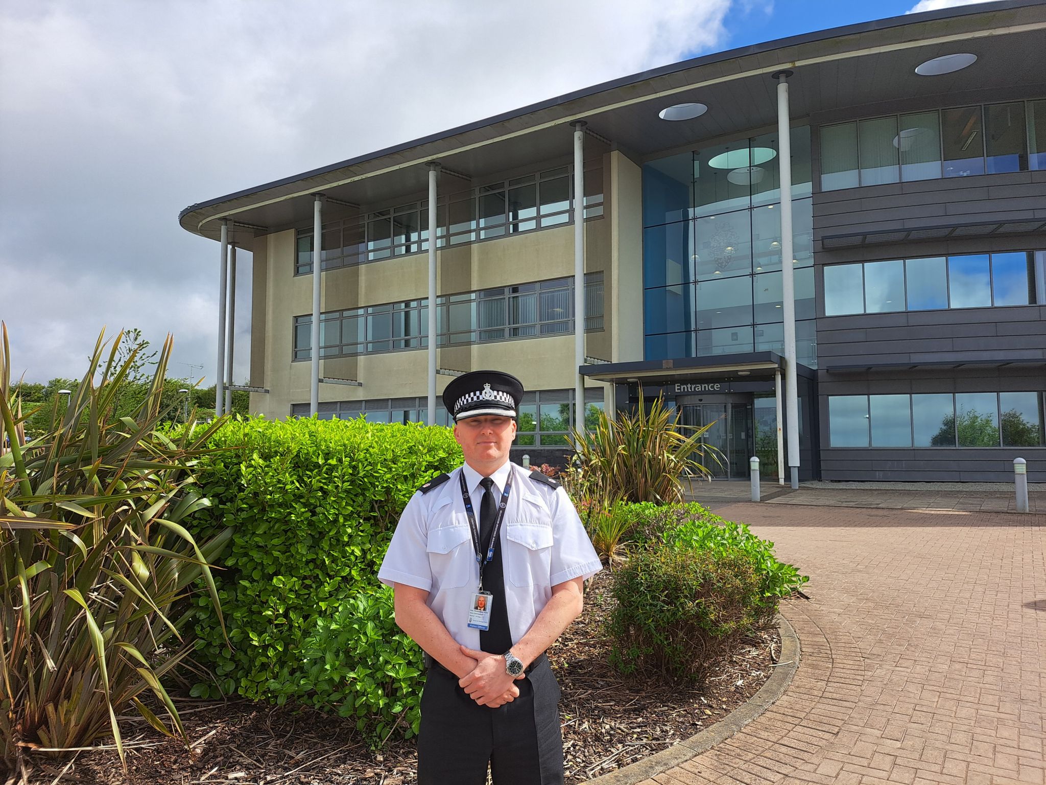 Police officer stood in front of bushes and building