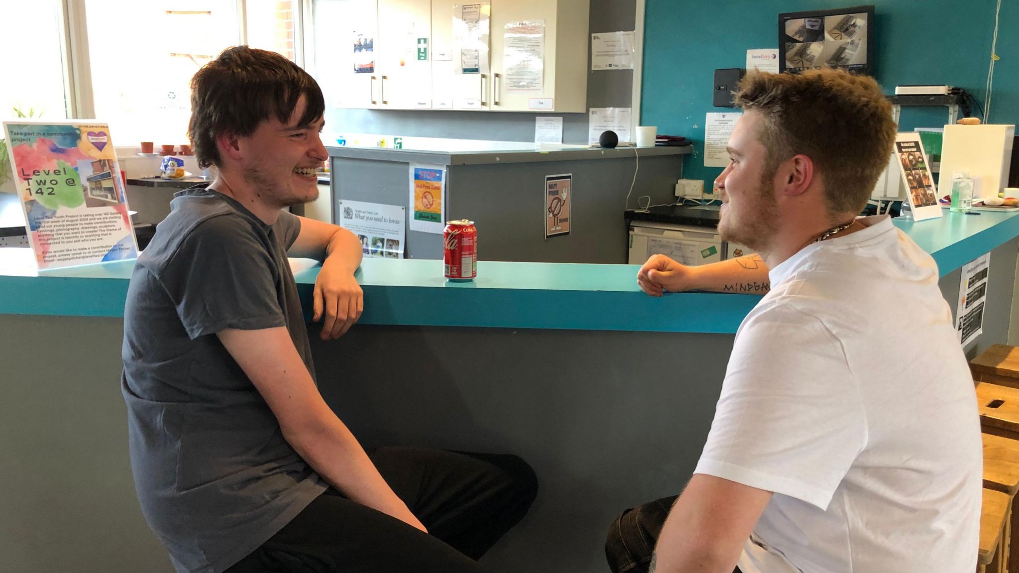 Two young men sit by a coffee bar talking and smiling