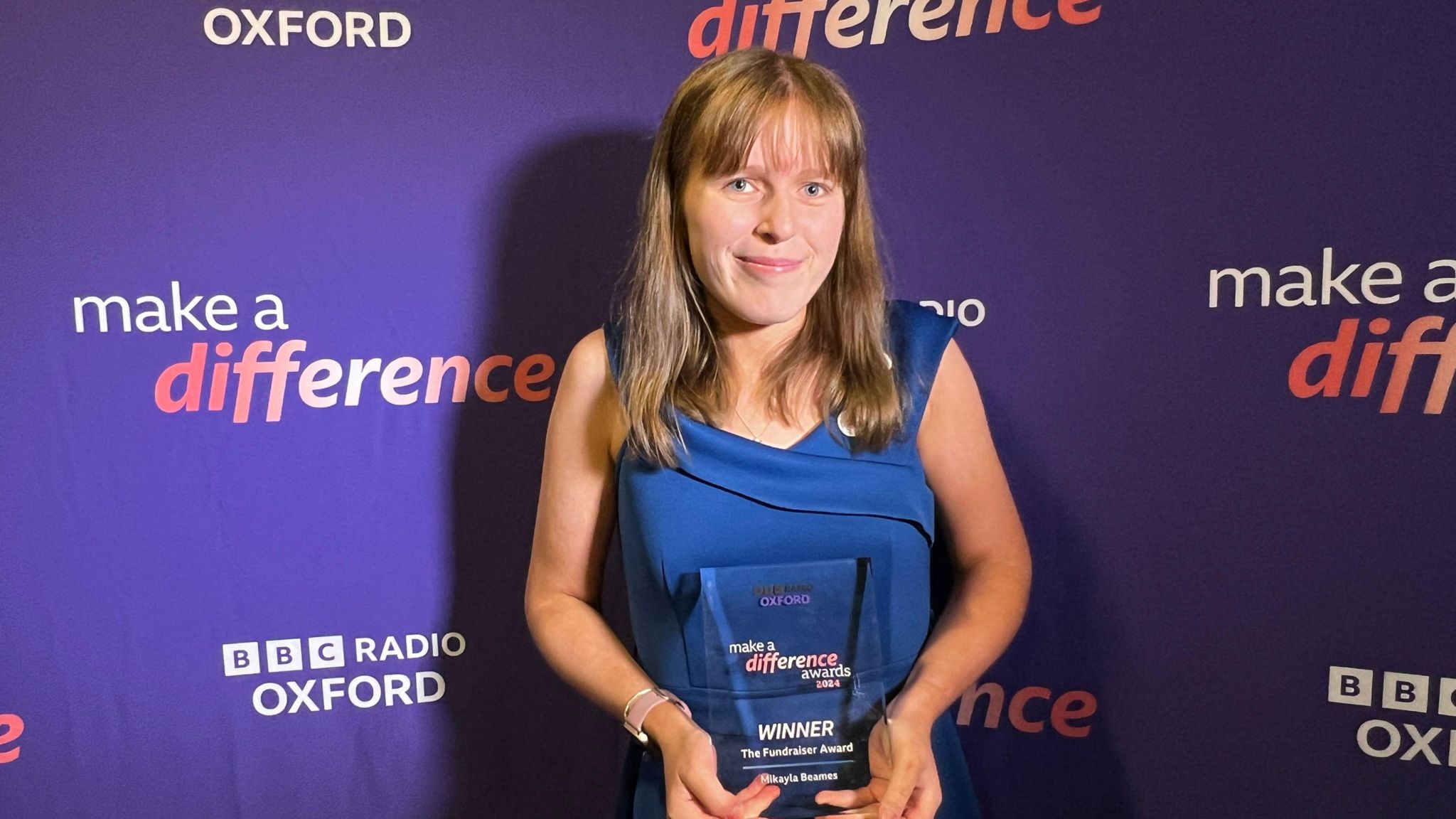 Mikayla Beames standing in front of a purple make a difference background and holding an award