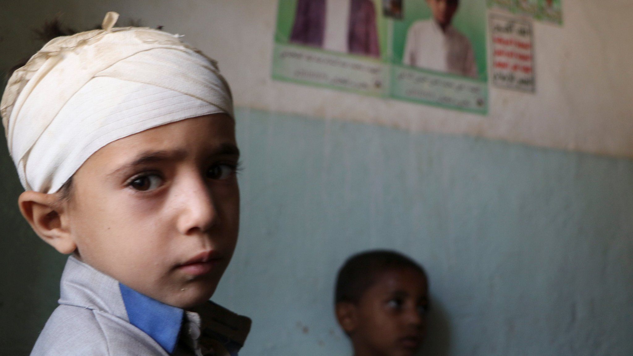 A boy injured in a Saudi-led coalition air strike on a bus in rebel-held Yemen stands next to posters of other boys who were killed (4 September 2018)