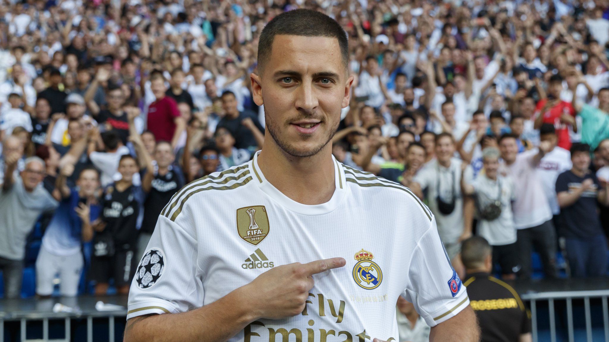 Eden Hazard points at the Real Madrid badge on his shirt following his unveiling at the Bernabeu in June