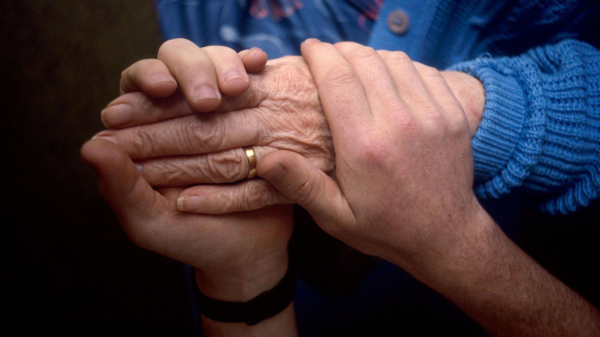 The hand of an elderly person being held by the hands of a younger person