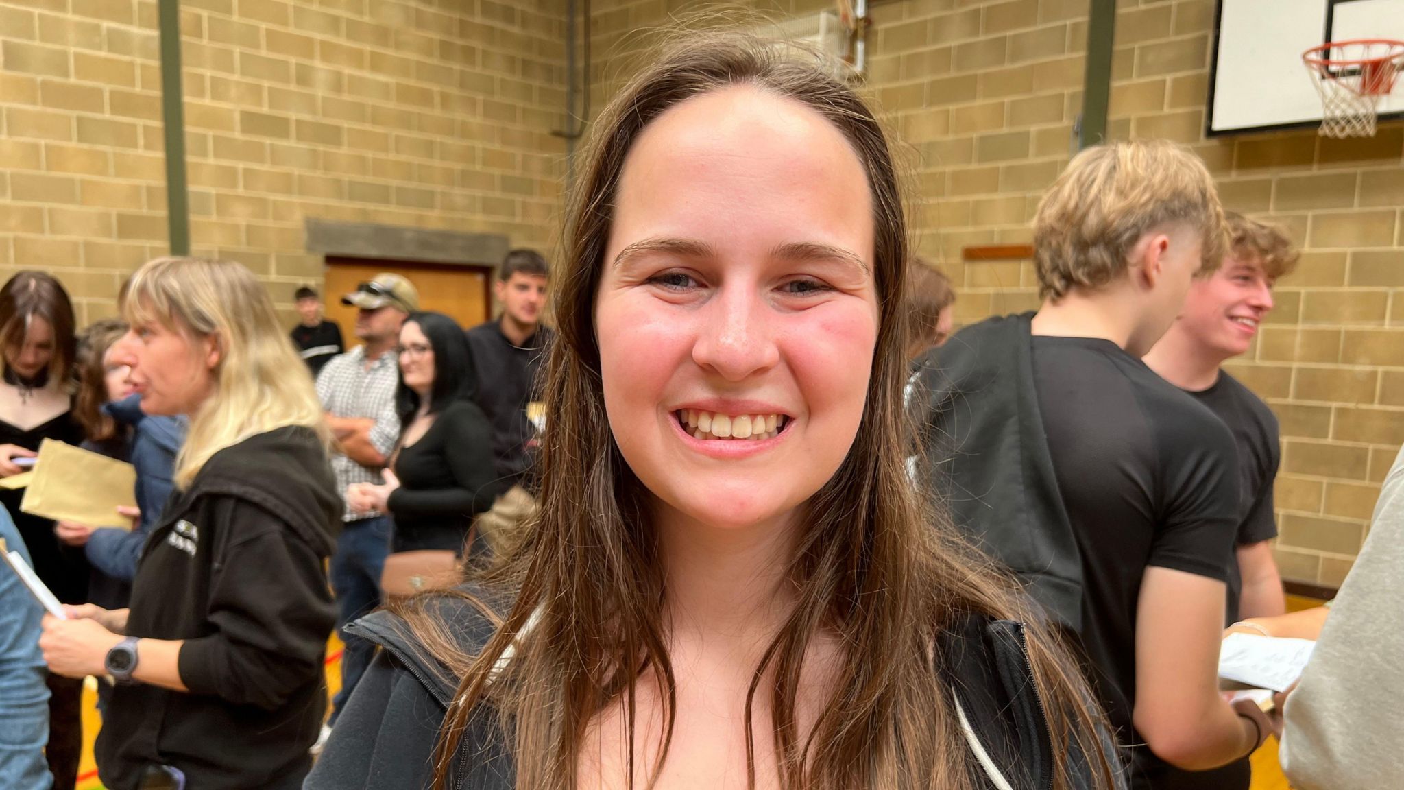 Erin smiling with pupils holding their results behind her in a school sports hall.