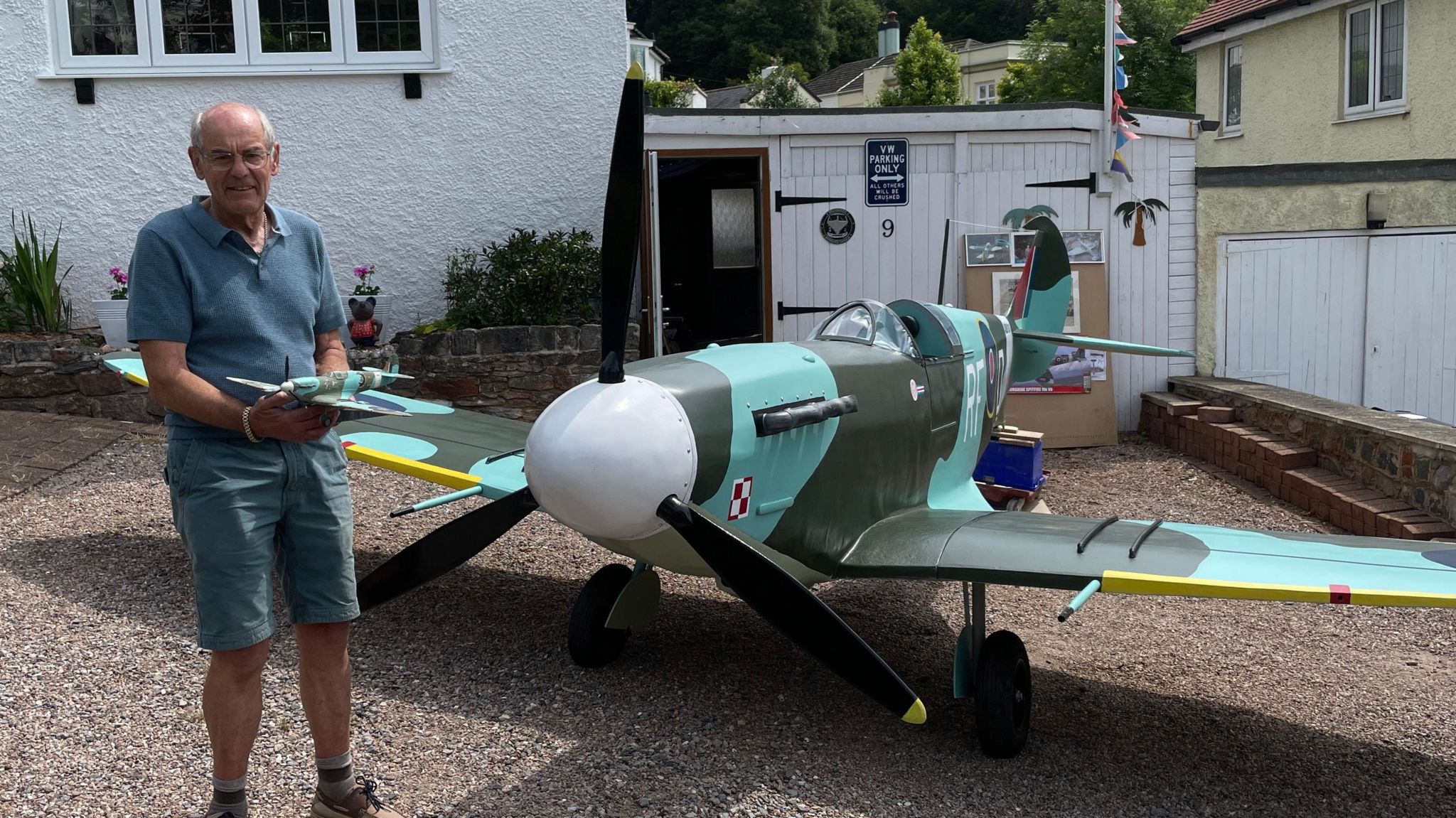 A man stands beside an almost full scale Spitfire aeroplane holding a 3/4 scale model