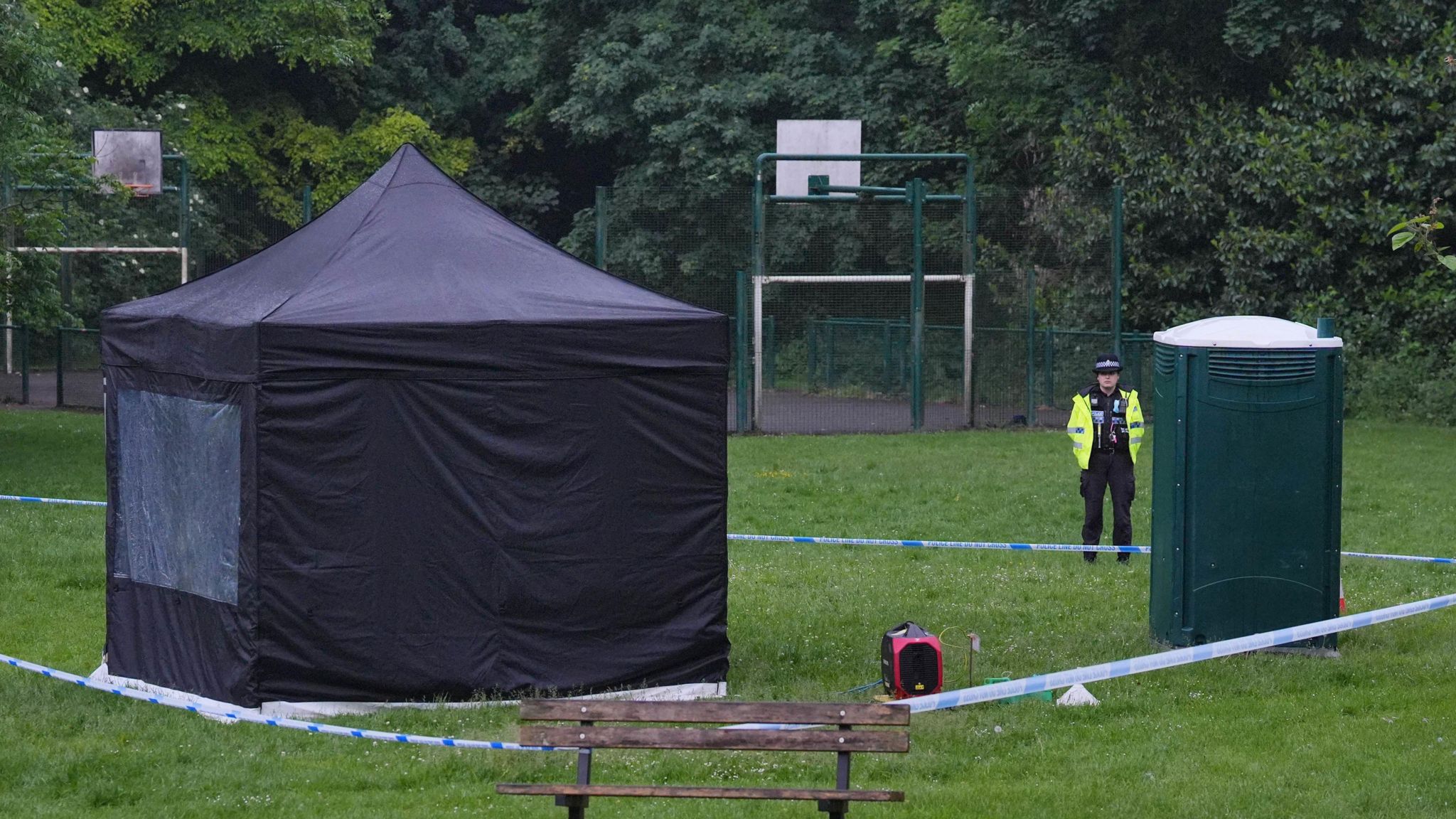 A black forensics tent seen in the middle of a park inside an area cordoned off by police tape
