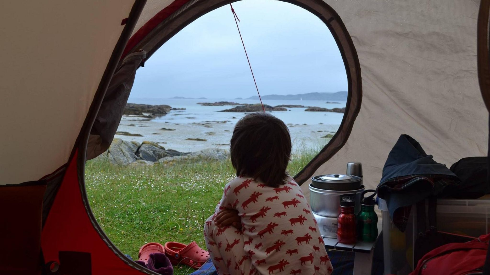 Finn sat in a tent looking out to the sea.He is wearing white pjs with red animal print on them