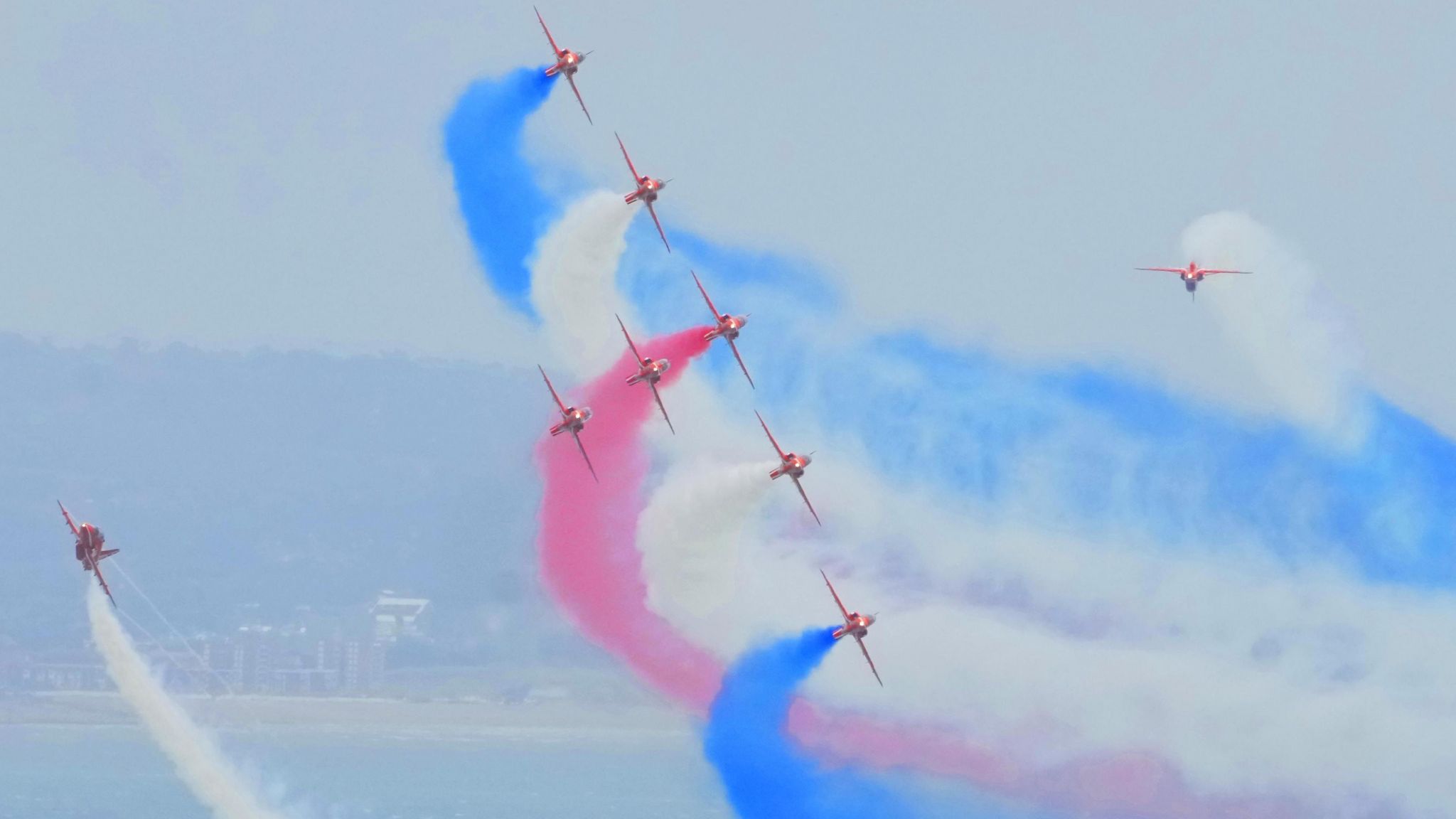 Planes fly at an angle with blue, white and red vapour trails behind them.