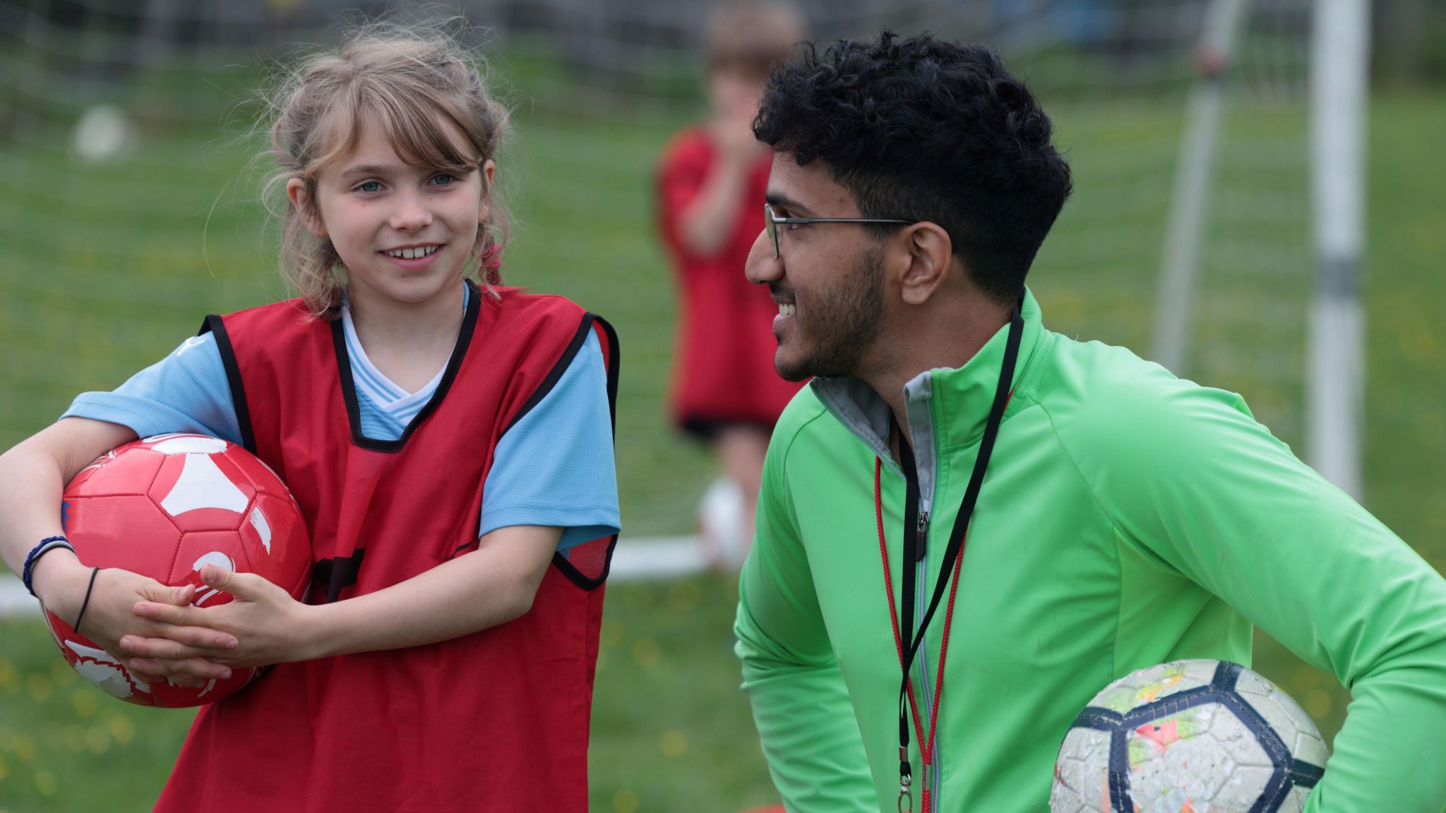 Girl holding football with man coaching in green jacket