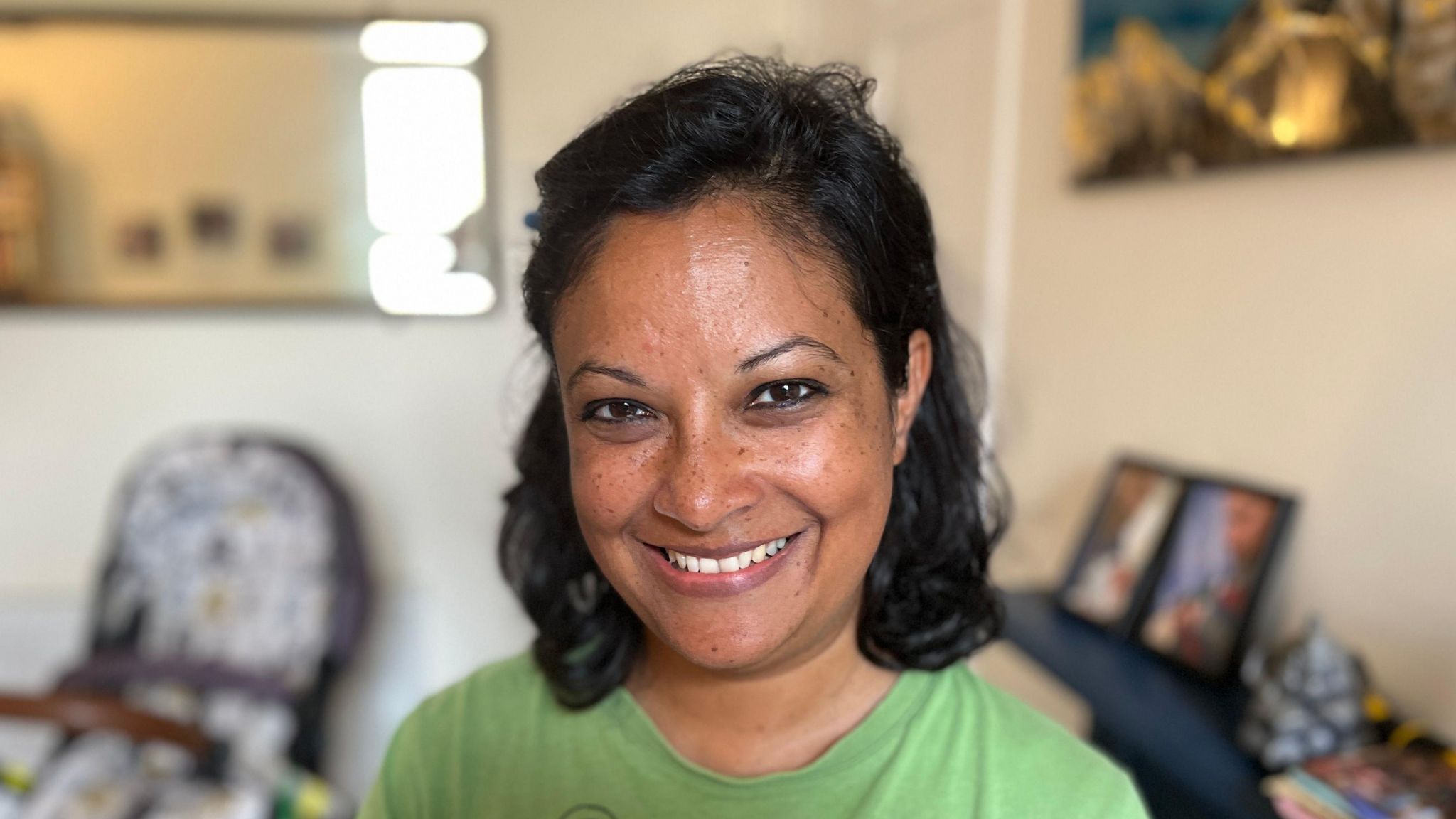 Isheeta Mustafi is a mother of Indian origin. She has short dark hair, wears a green t-shirt and is smiling at the camera.