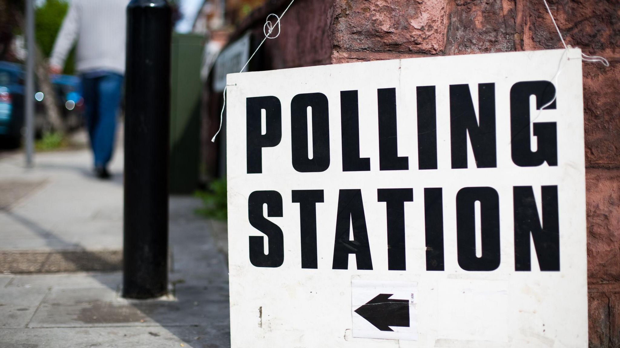 A white polling station sign with an arrow pointing tothe left