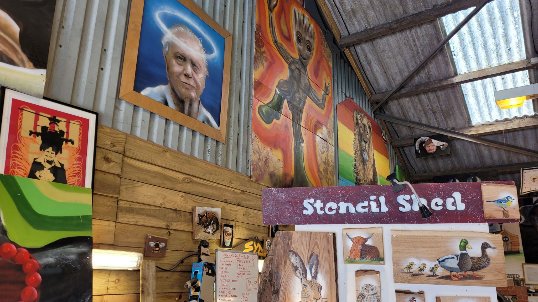 The inside of Stencil Shed with various artworks on display including one of David Attenborough with a halo above his head