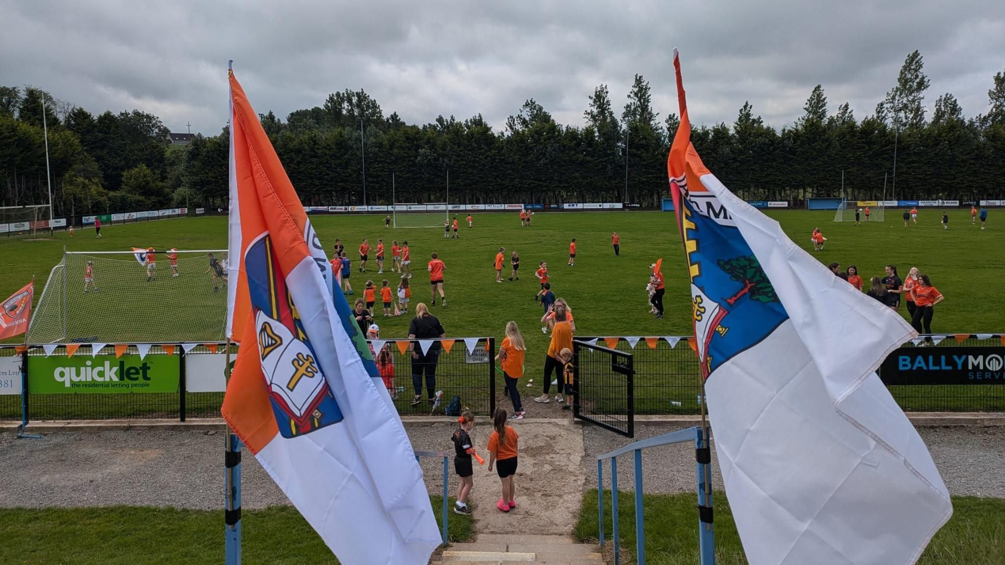 GAA pitch with lots of kids on it, flags in the foreground