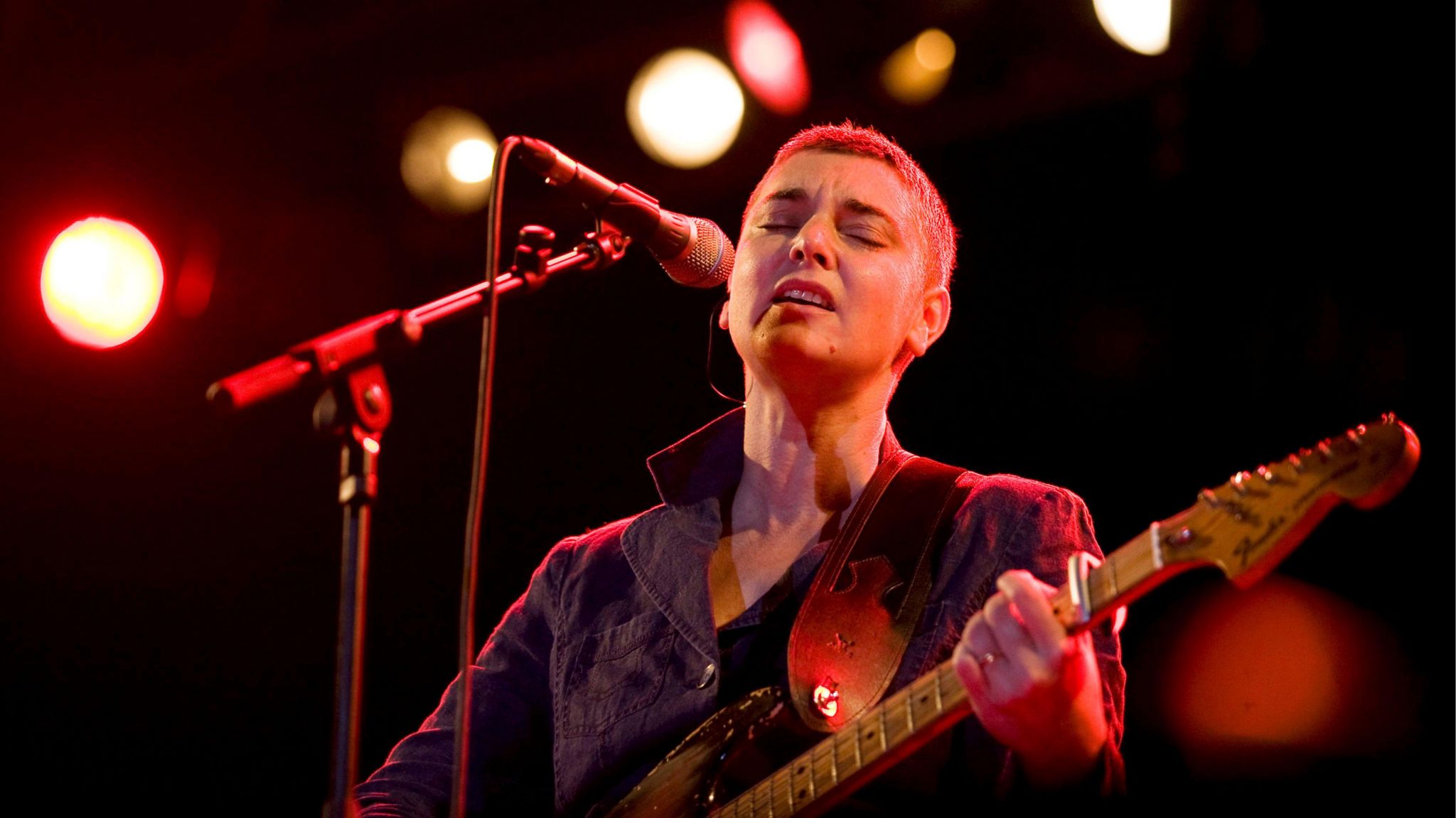 Sinéad O'Connor singing on stage with a guitar