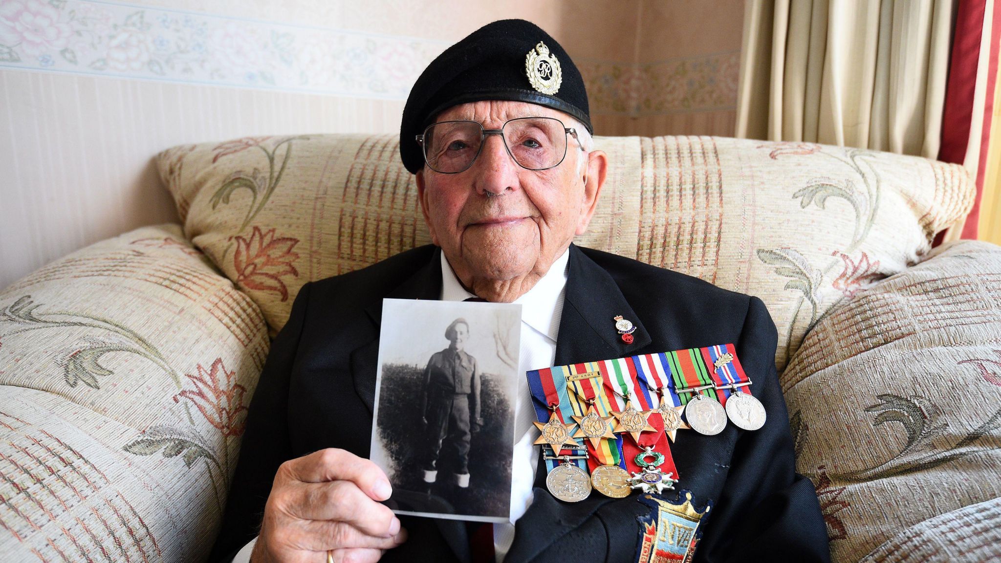 Don Sheppard wearing his military medals holding a photo of himself as a young soldier