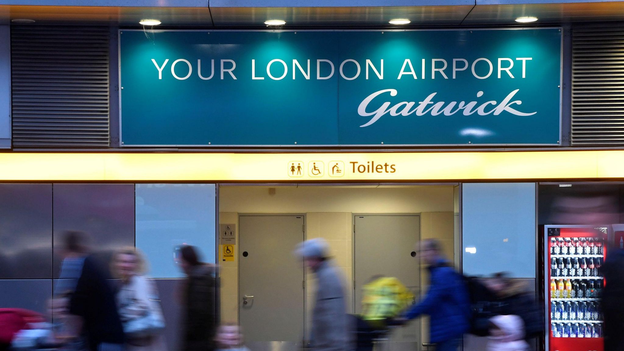 Passengers walk past a sign welcoming them to Gatwick Airport