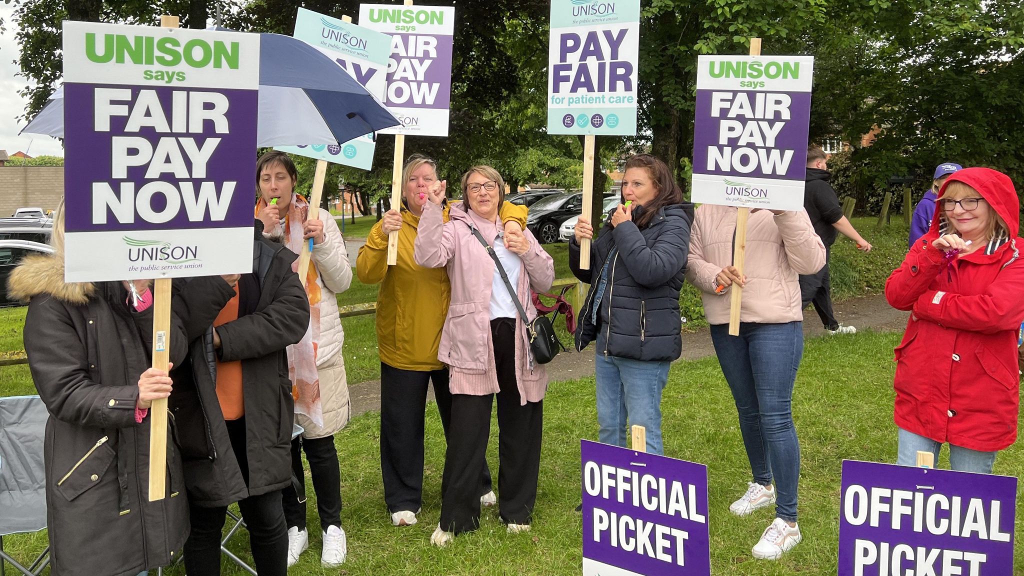 Staff holding placards that read 'Pay Now'