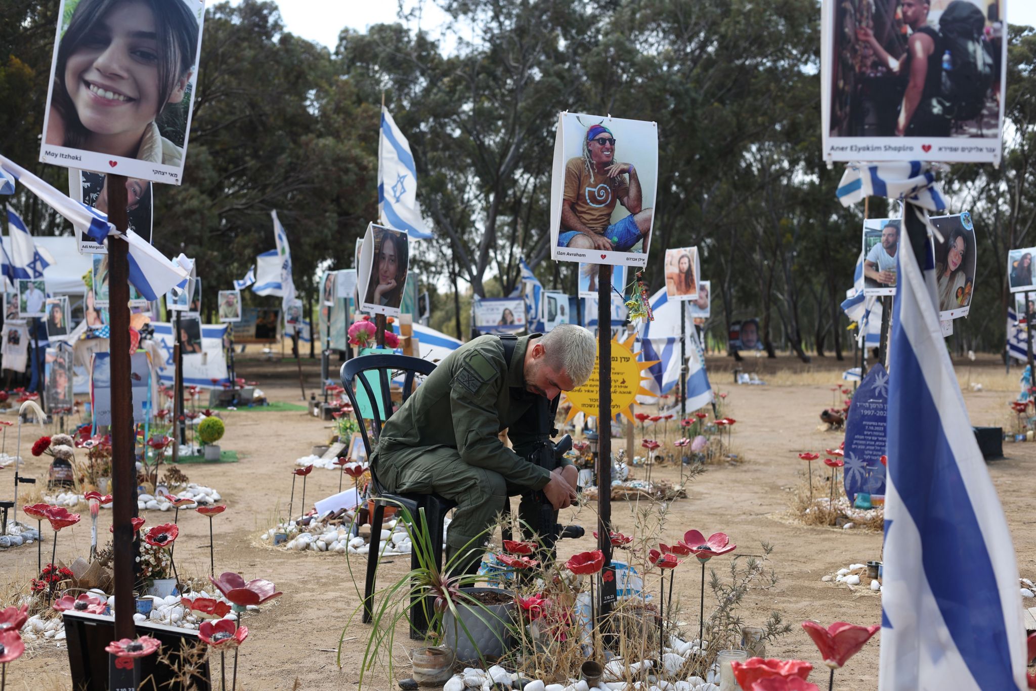 A man sitting on a chair at the memorial site where the Nova music festival attack took place - he is surrounded by Israeli flags and pictures of people who were killed