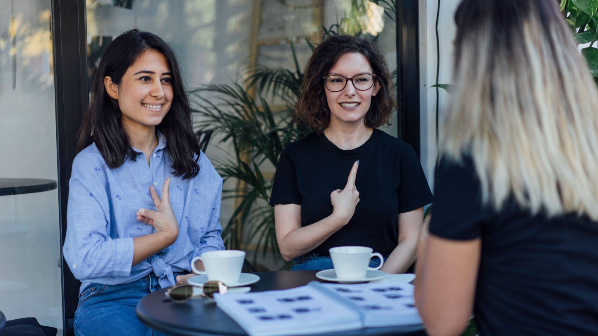 Three women sat at a table communicating through sign language. 