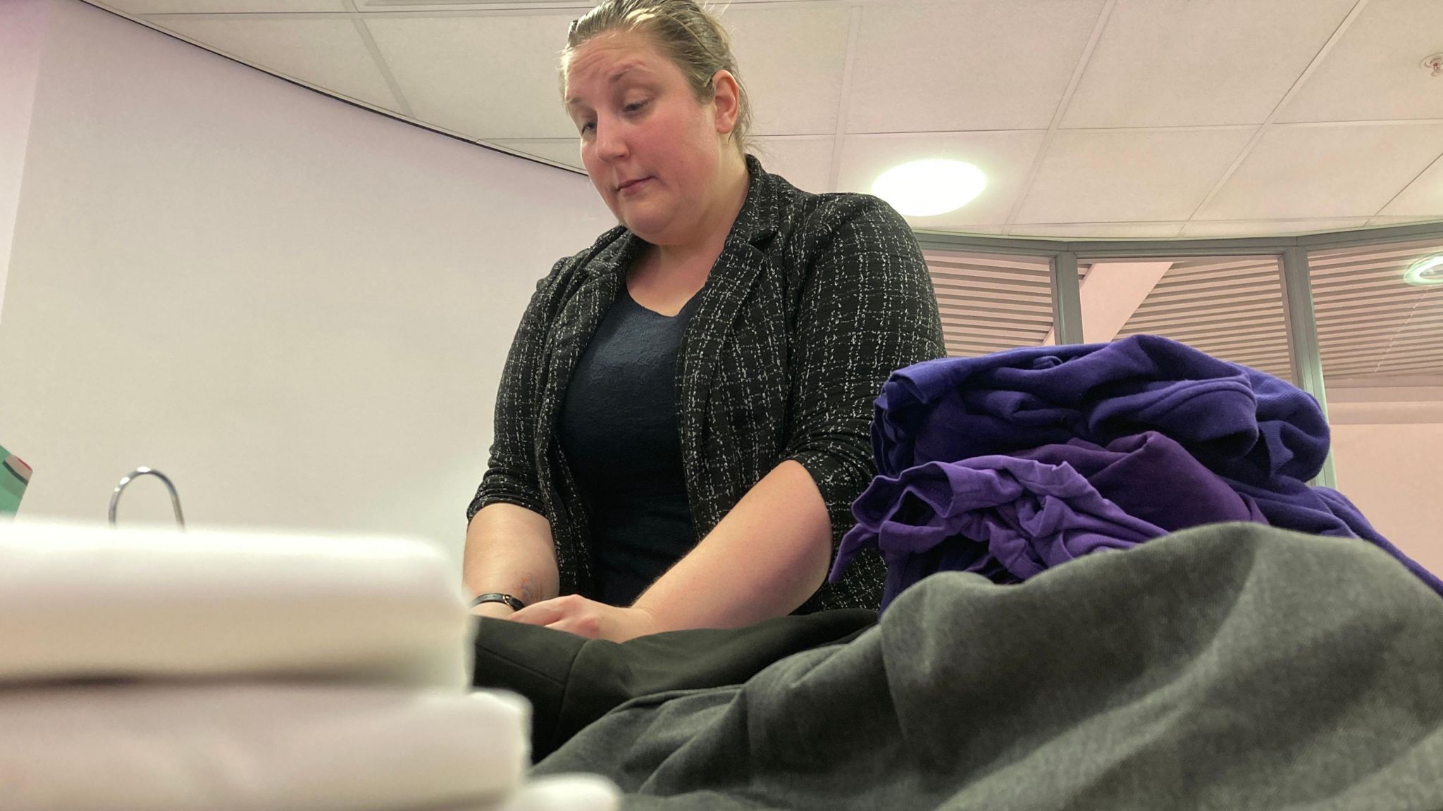 Marketing manager Gemma Hyde sorts through clothing in a room, surrounded by piles of donated school uniforms