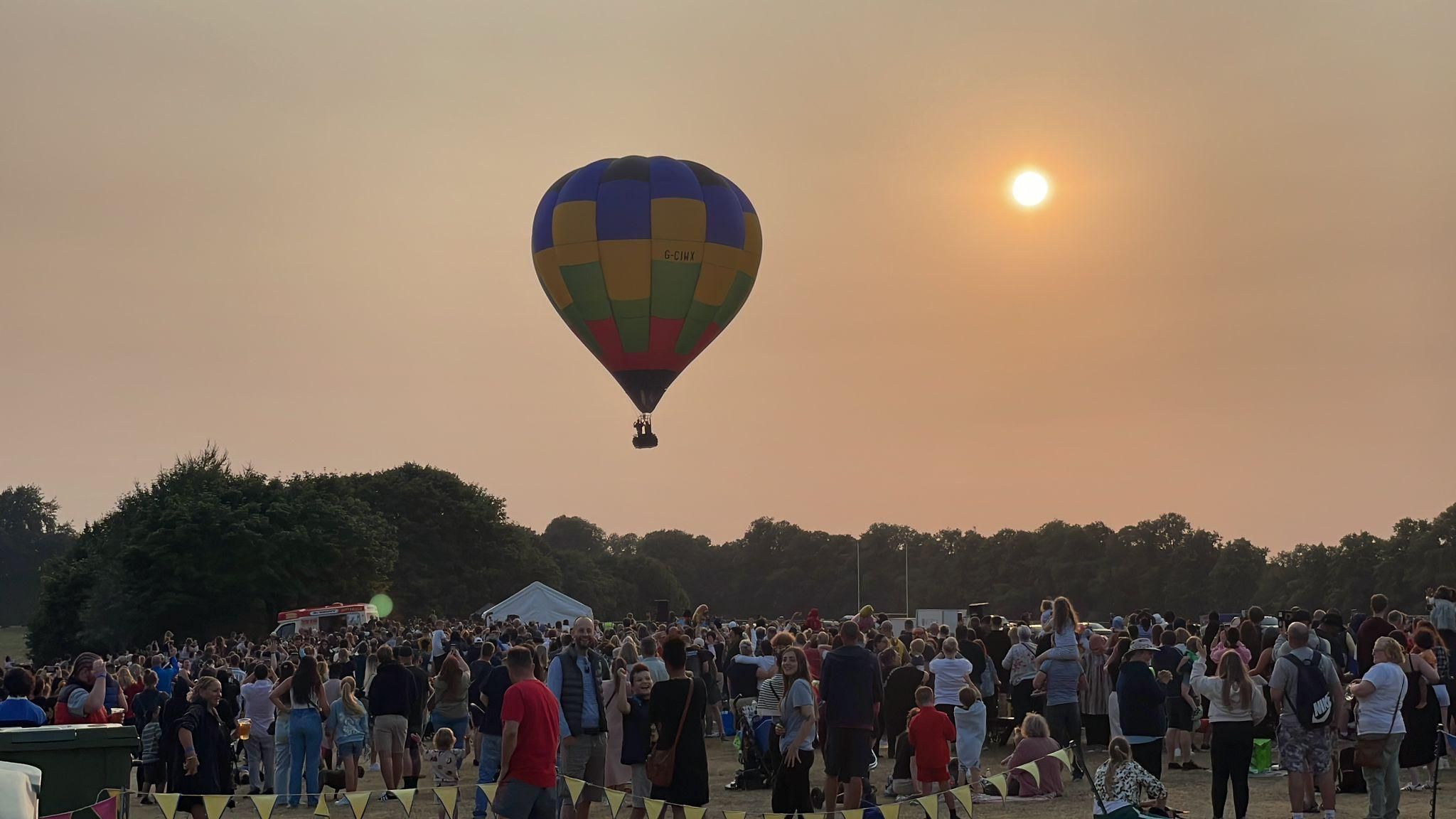 Hot air balloon in flight over Northampton's Racecourse park as a crowd watches on