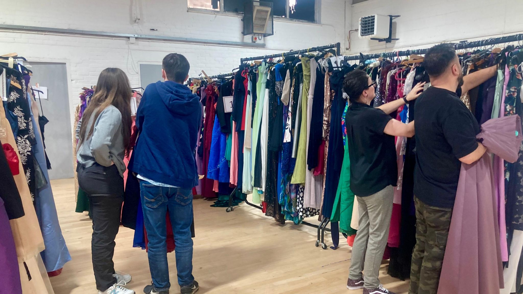 Four people looking through racks of ball or prom dresses at an event in Harlow