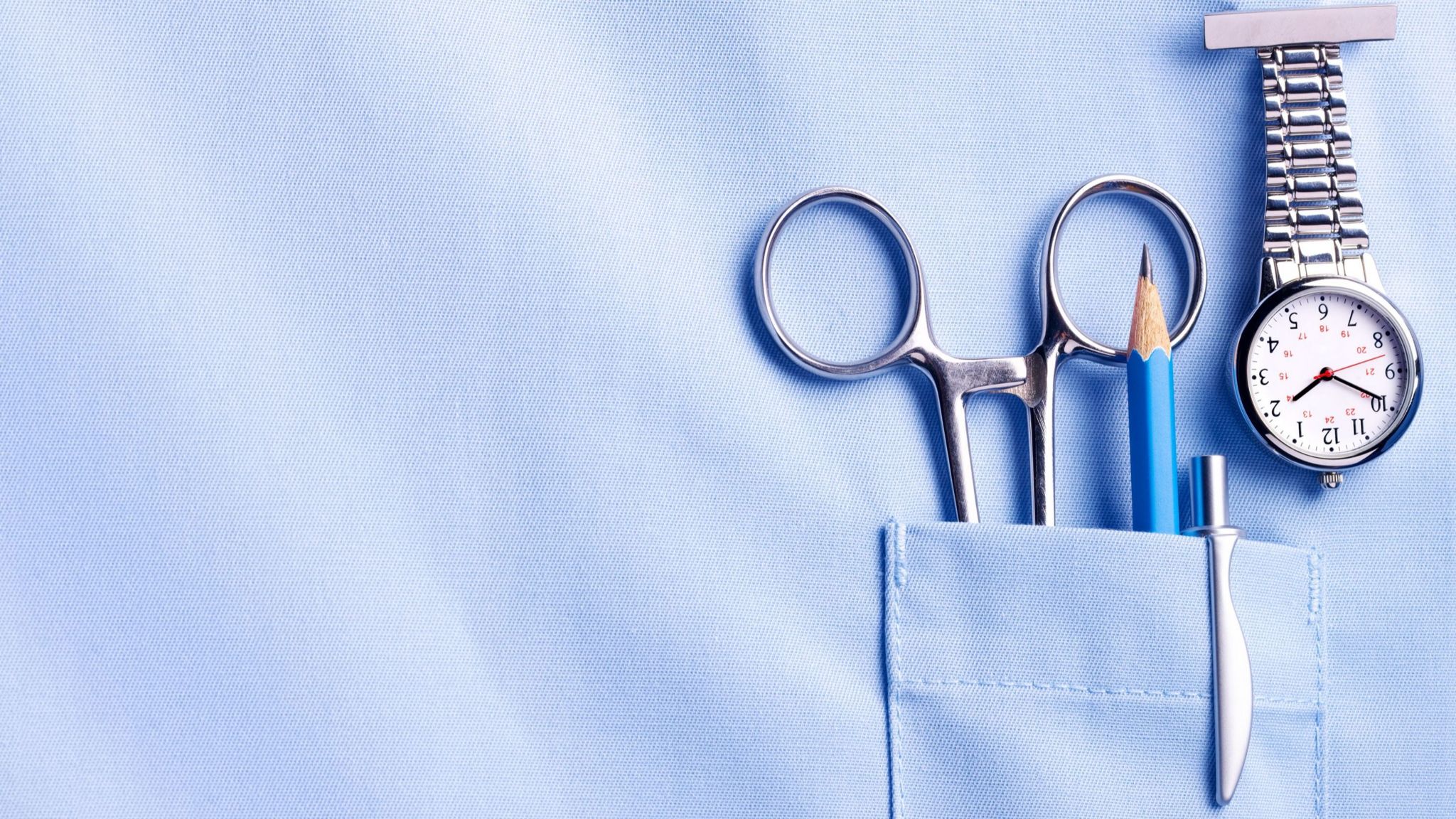 Close up of a scrubs pocket with a pencil, pen, scissors and a watch.