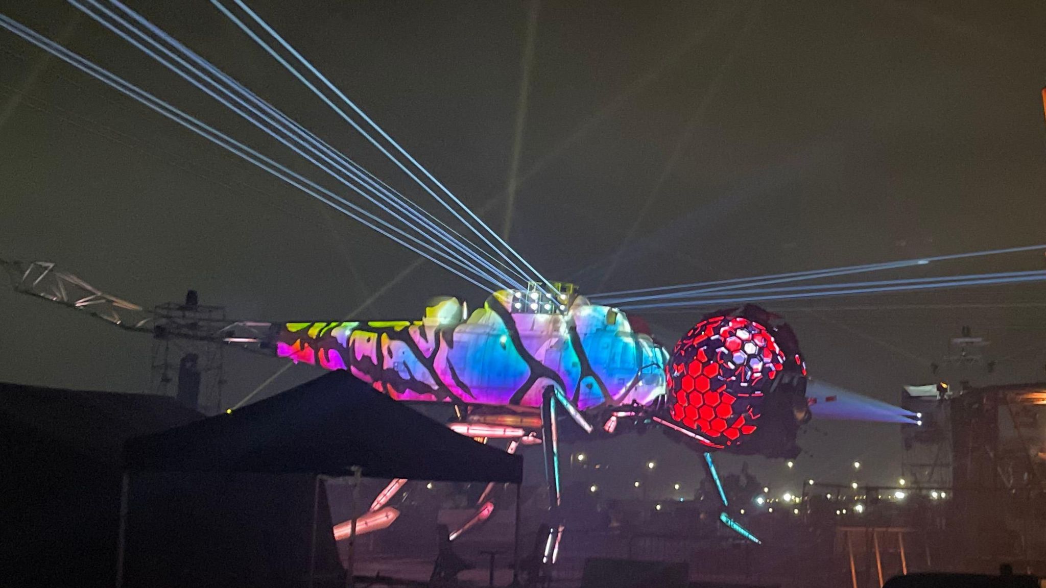 A mechanical Dragonfly lit up at night at Glastonbury Festival in blue, purple, and red colours.