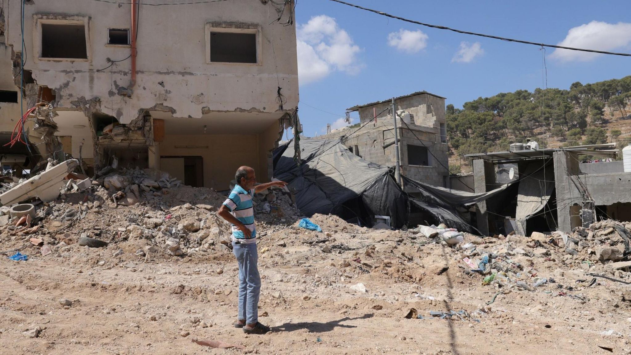 A man gestures towards buildings and tarmac destroyed by Israeli bulldozers and ground forces in Tulkarm, in the occupied West Bank, following a two-day Israeli army operation (30 August 2024)