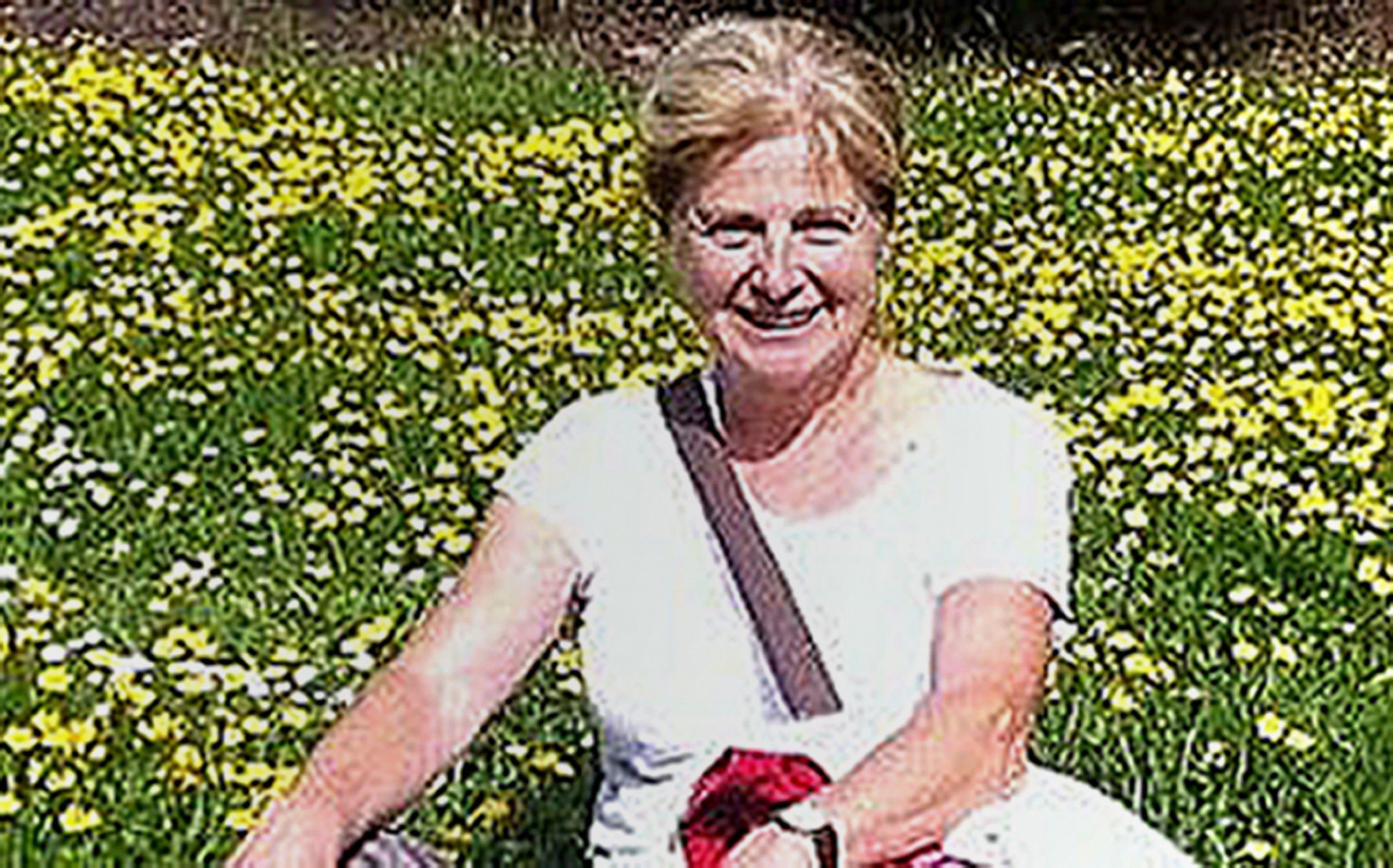 Danielle Carr-Gomm pictured wearing a white t-shirt, sat on the ground amongst lots of yellow flowers. 