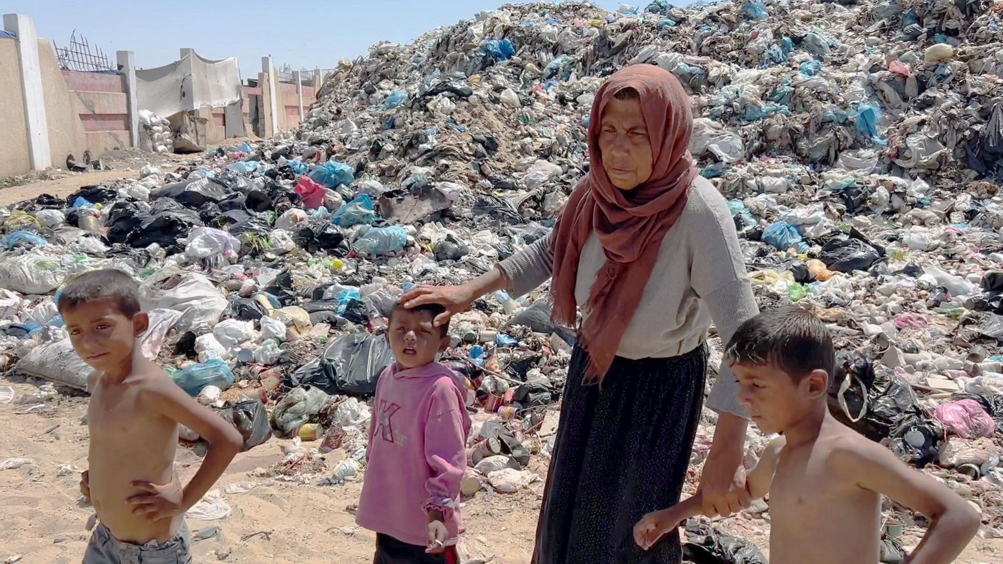 Asmahan stands with three of her grandchildren in front of a giant rubbish heap