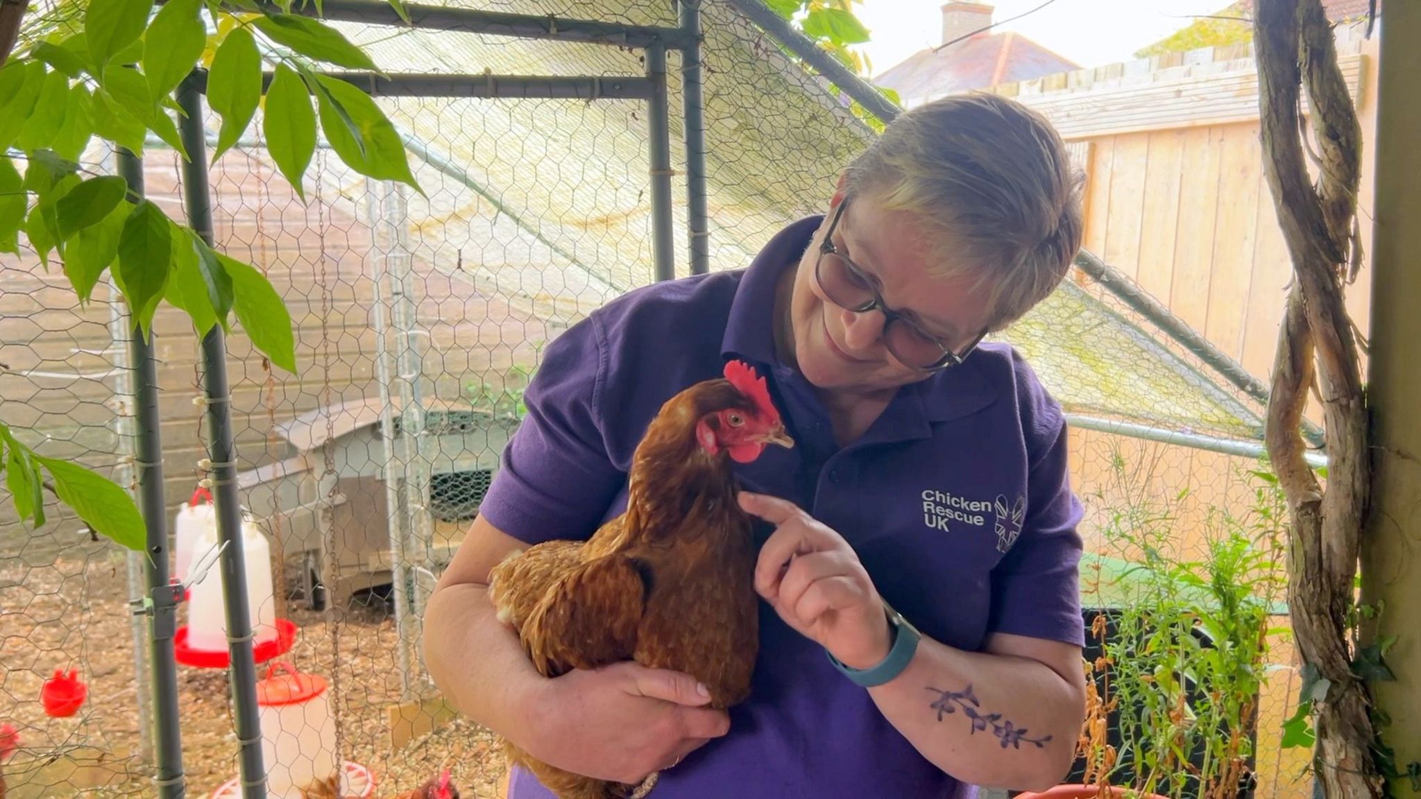 Jenny Betts with short fair hair wearing a purple top and carrying a brown hen