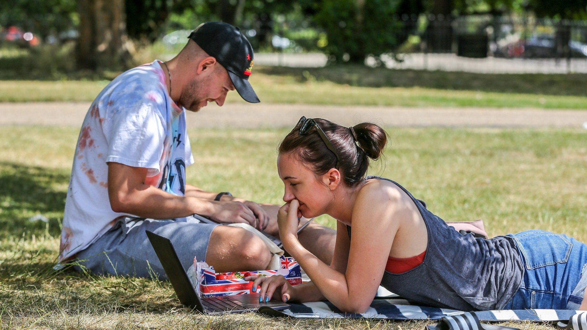 A couple seen working on their laptops under the shade on a hot and sunny day London