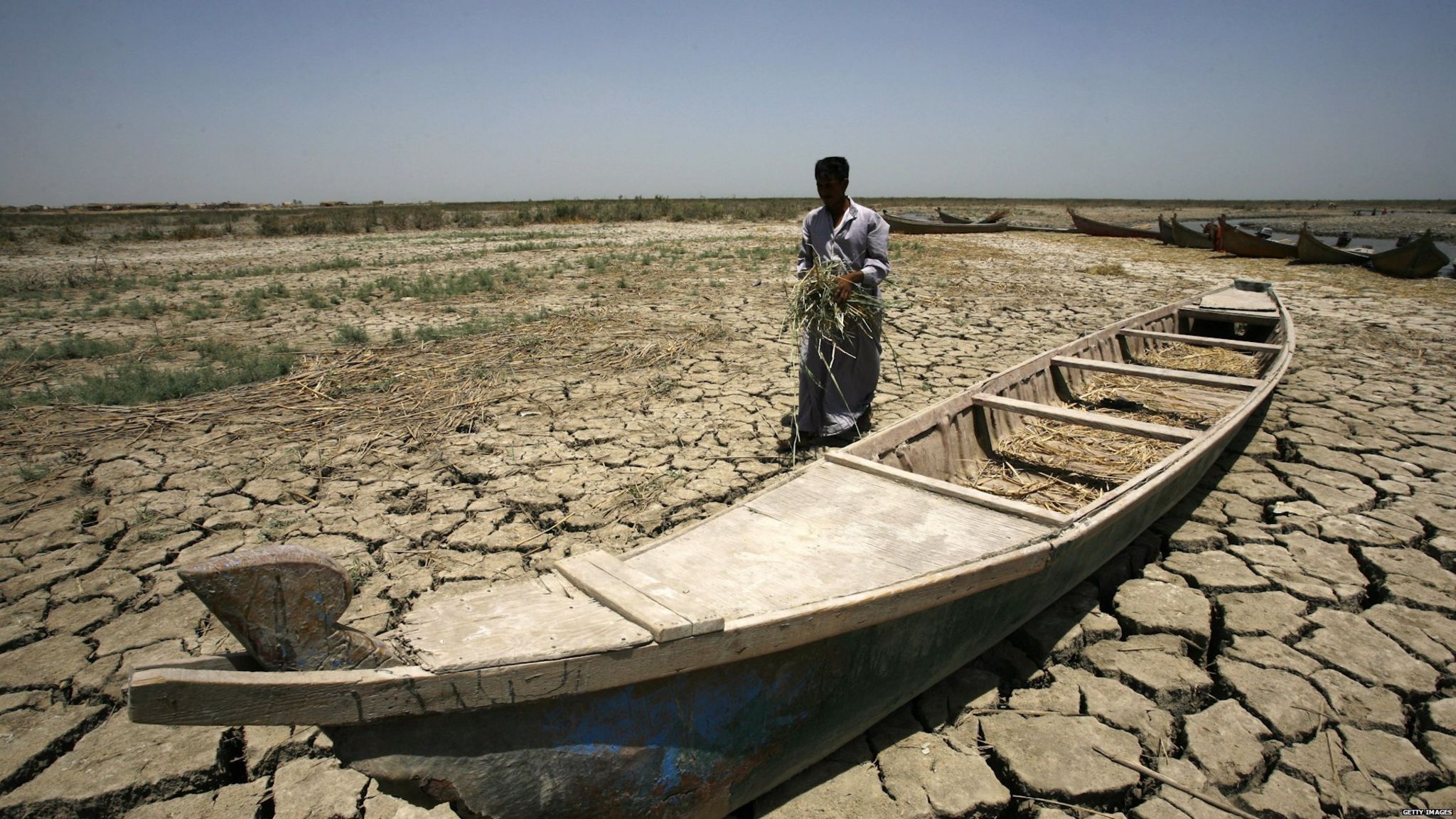 An Iraqi man walks past a canoe siting on dry, cracked earth in the Chibayish marshes near the southern Iraqi city of Nasiriyah