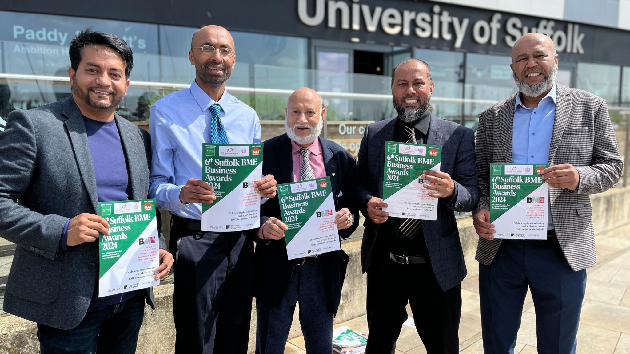 Five men of Bangladeshi heritage stand holding A4 posters promoting an awards event