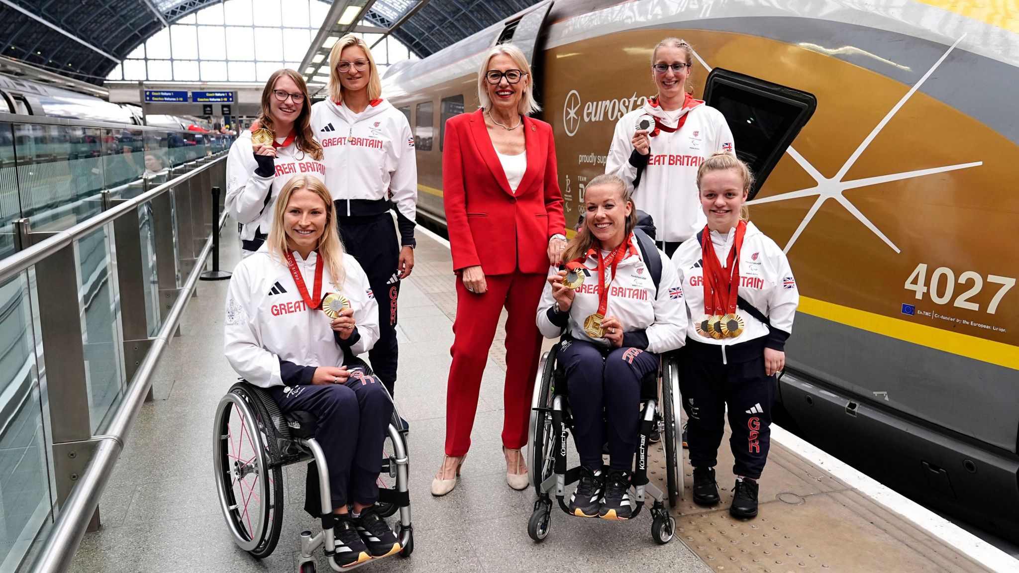 Eurostar CEO Gwendoline Cazenave stands in the centre of six Paralympians including Hannah Cockroft (front row, second right) and Maisie Summers-Newton (right). The athletes are wearing Great Britain team hoodies and tracksuit bottoms, and some are wearing or holding up medals. They are on a platform at London St Pancras, with a Eurostar train to the right