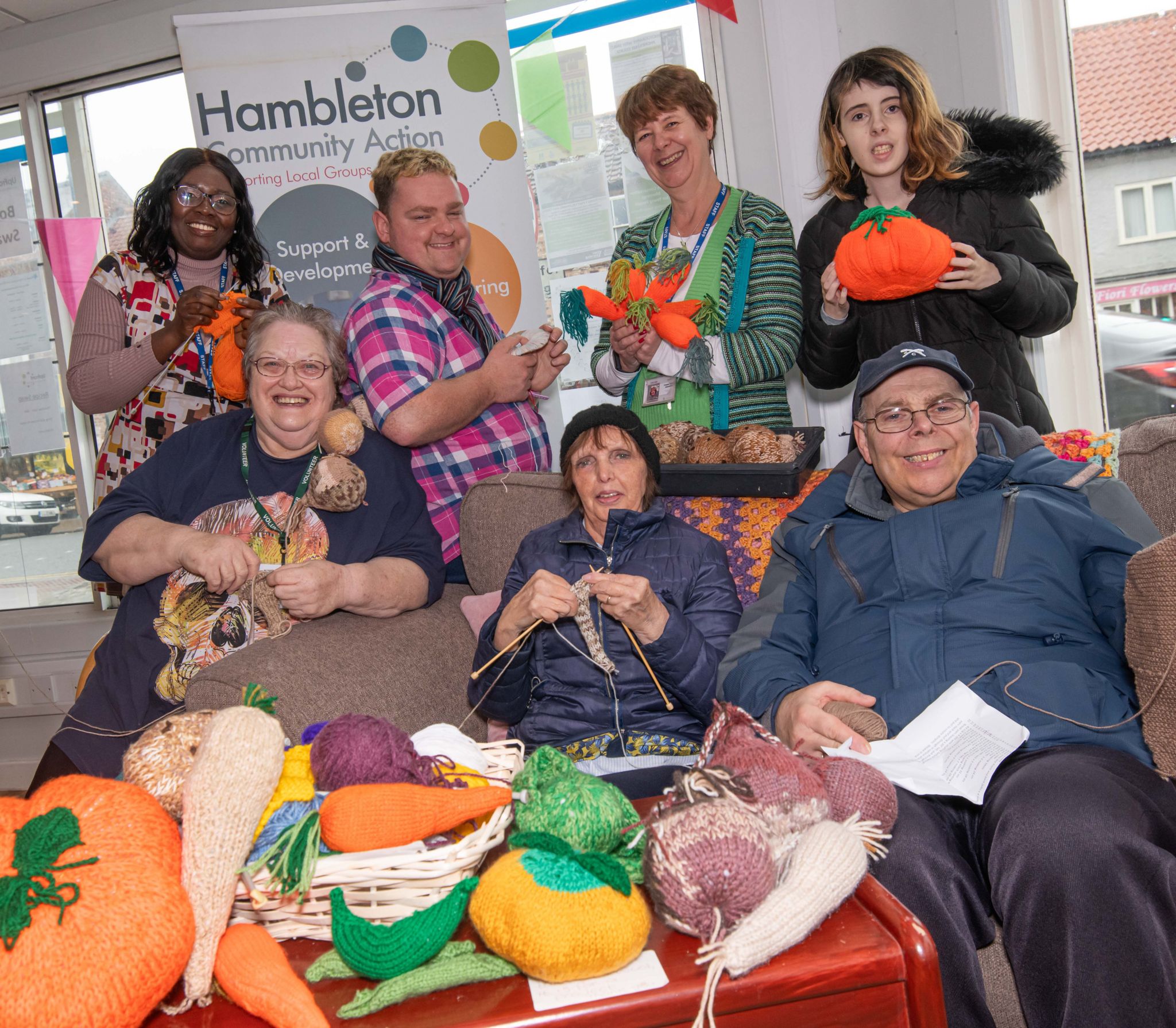 A group of knitters are pictured surrounded by knitted vegetables, including pumpkins and carrots