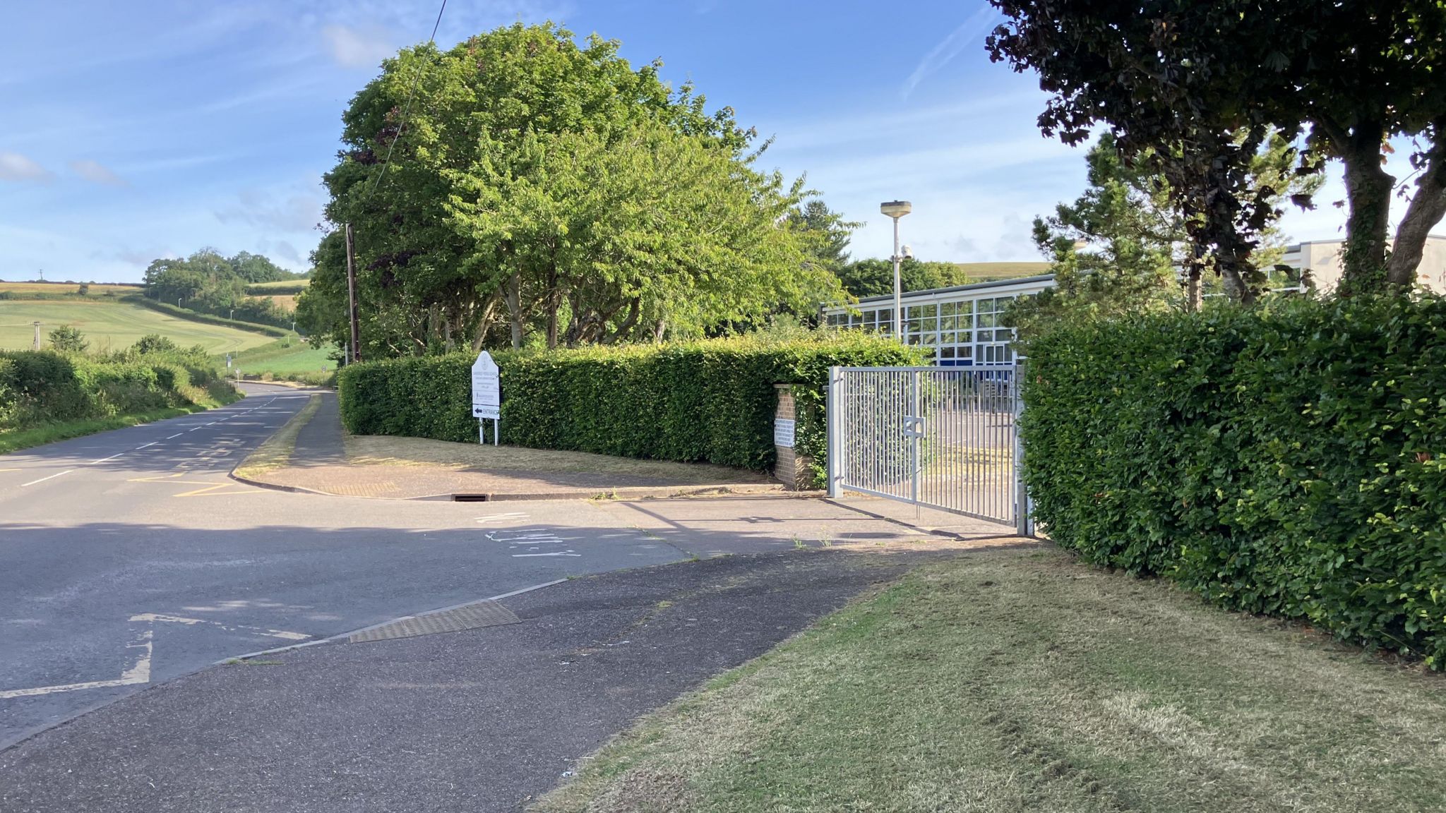 The closed gates of Danesfield Middle School in Williton next to a road, with fields in the background