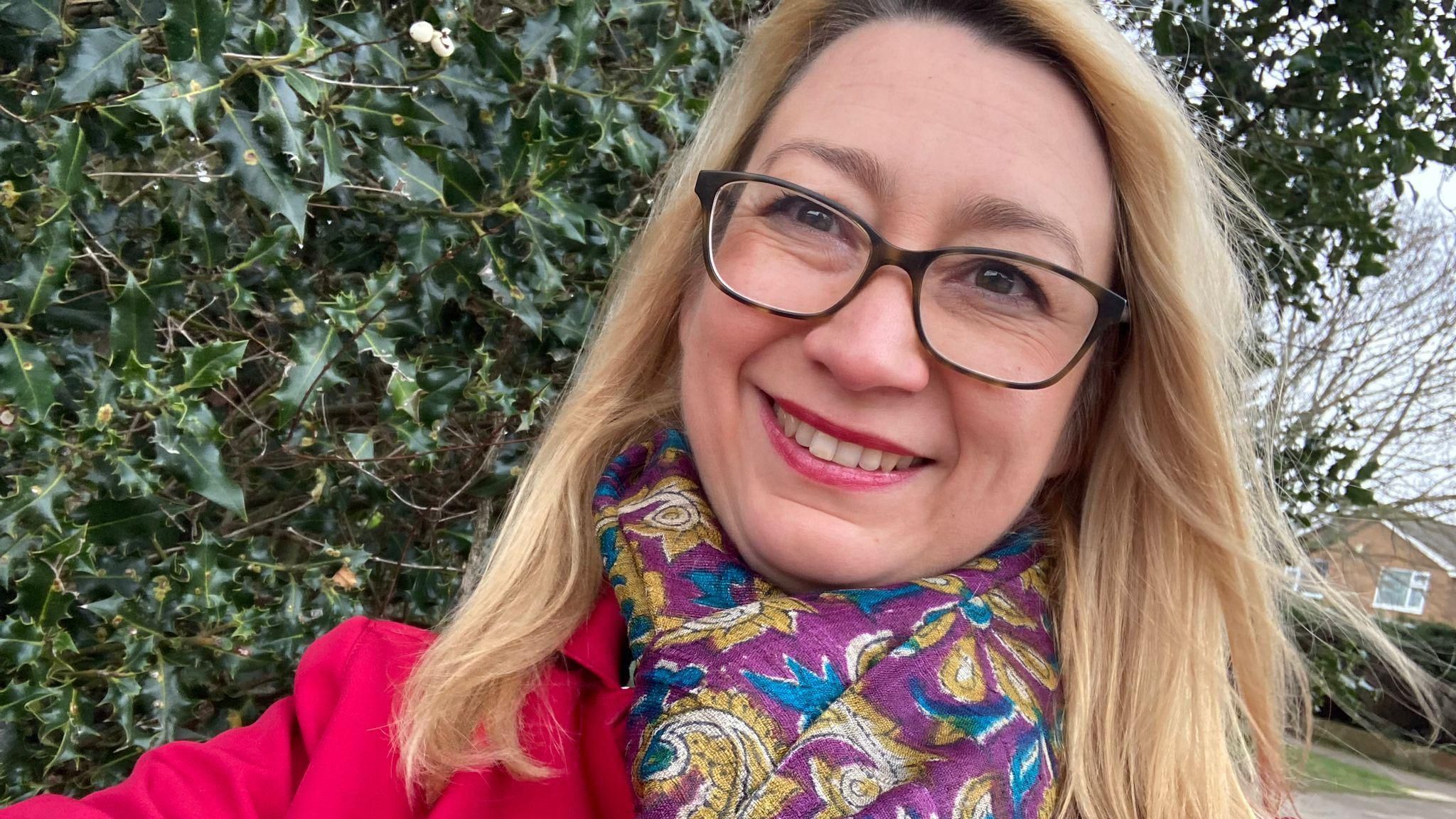 Jessica Asato poses for a selfie while wearing glasses and a purple patterned scarf