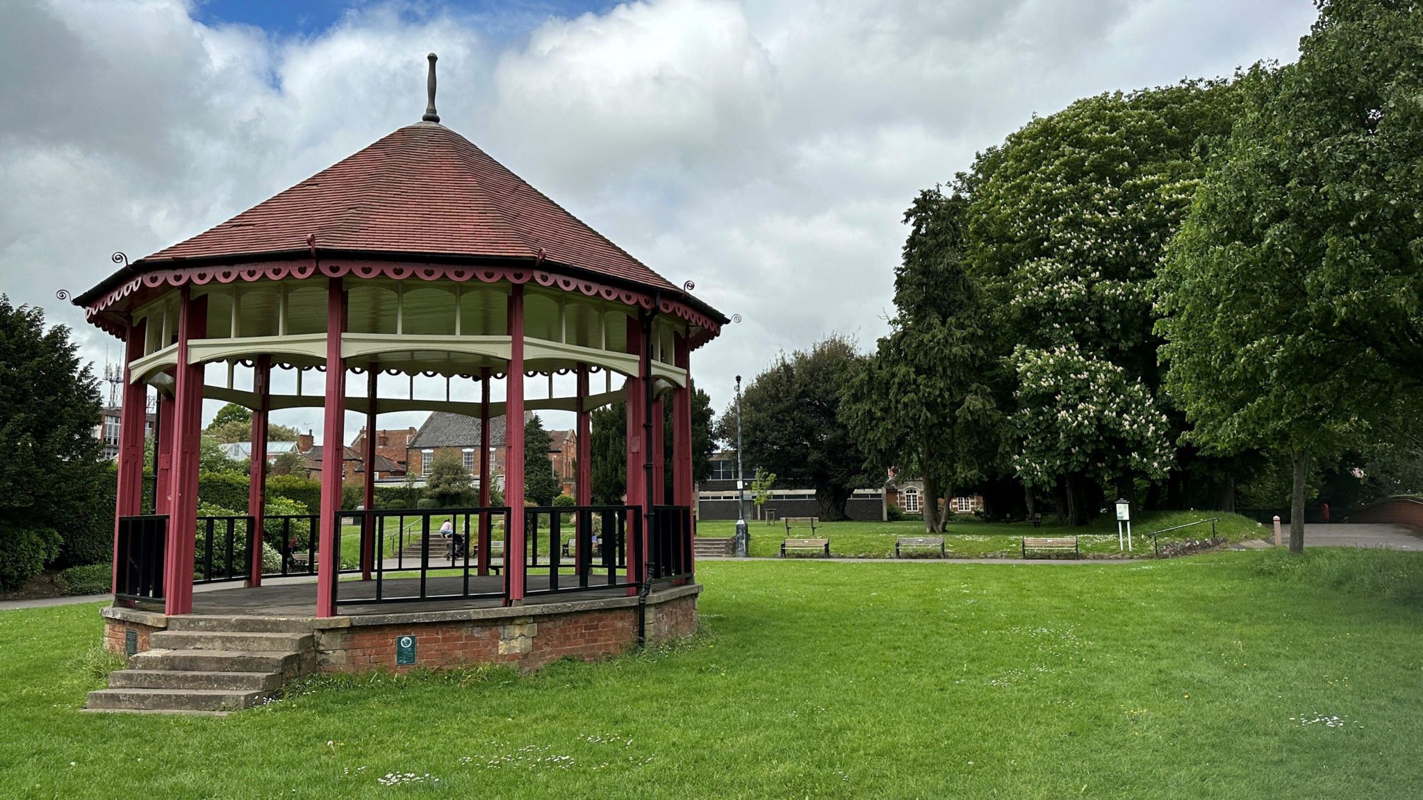 A bandstand in the middle of a green space surrounded by tall trees