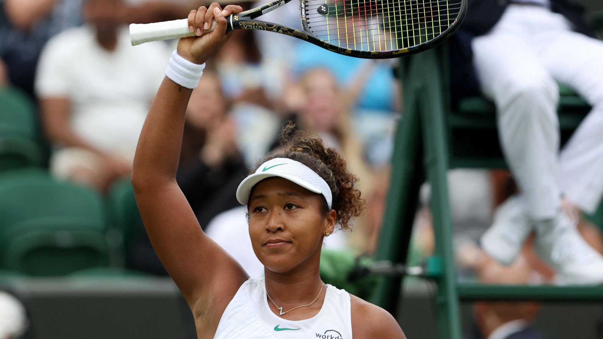 Naomi Osaka raises her racquet to the crowd after winning her first-round match at Wimbledon