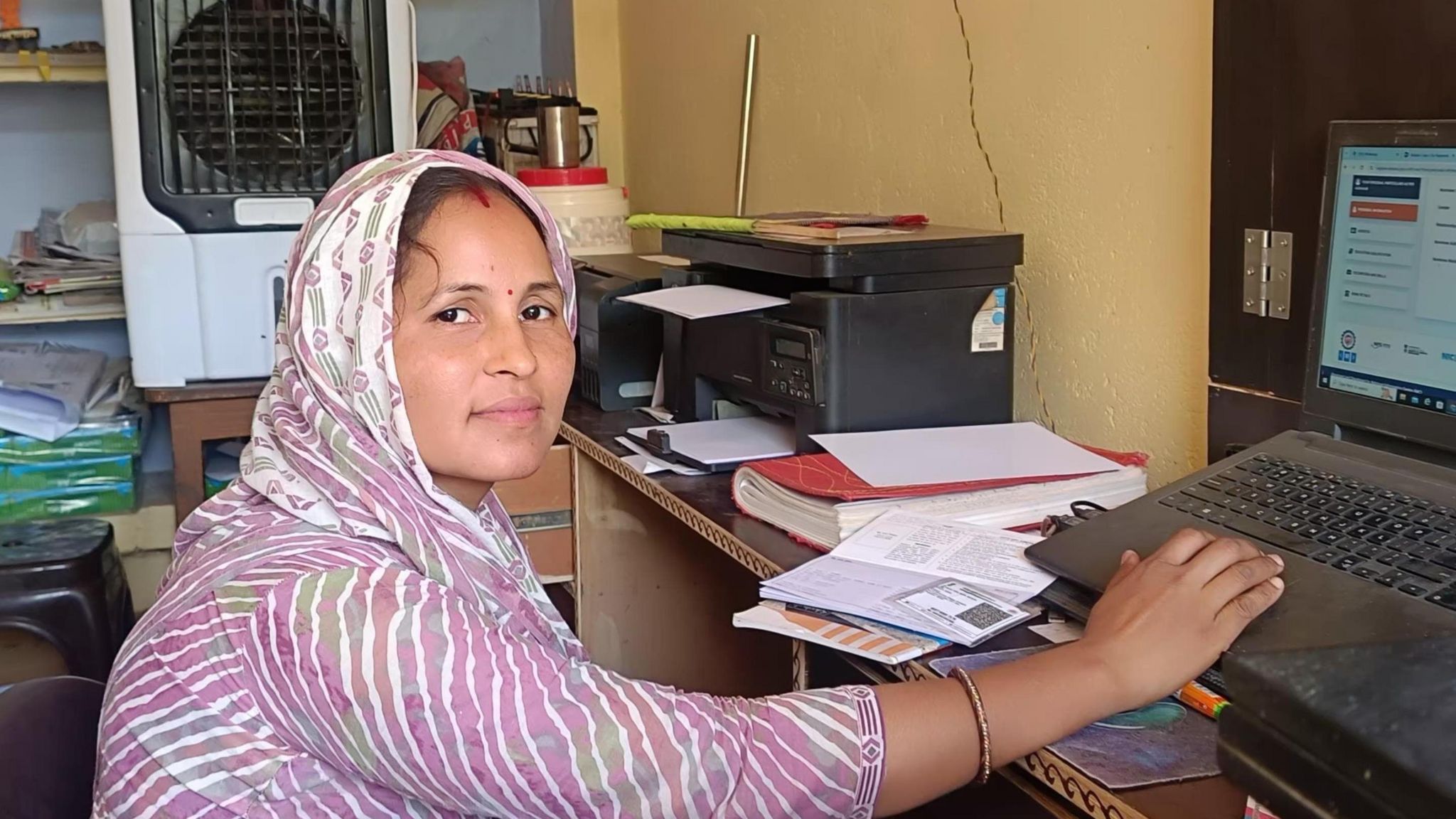 Poonam Untwal sits in front of her computer wearing a stripy pink dress and headscarf