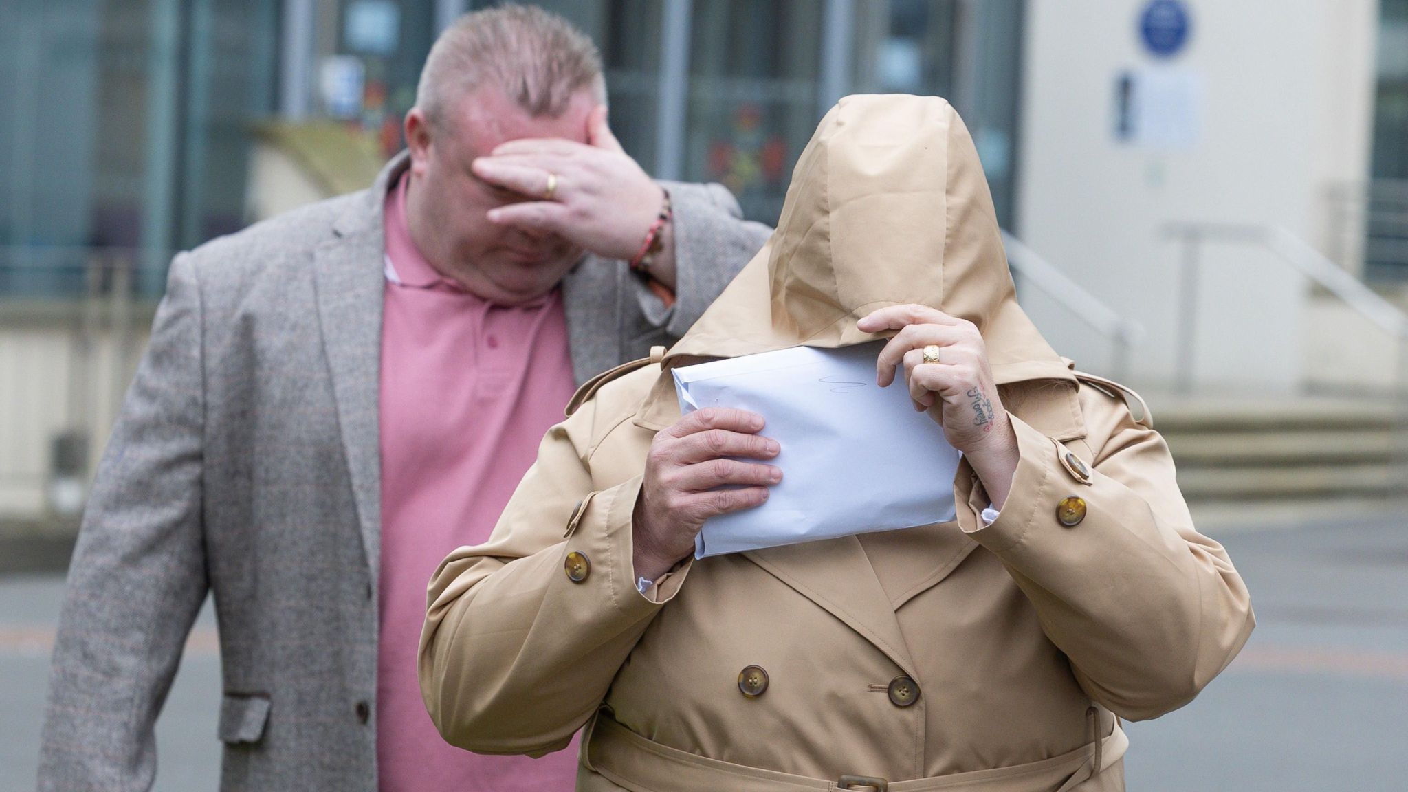 Bernard Mcdonagh in a pink shirt and grey jacket covering his face stood behind Ann McDonagh who is wearing a beige coat with a letter covering her face