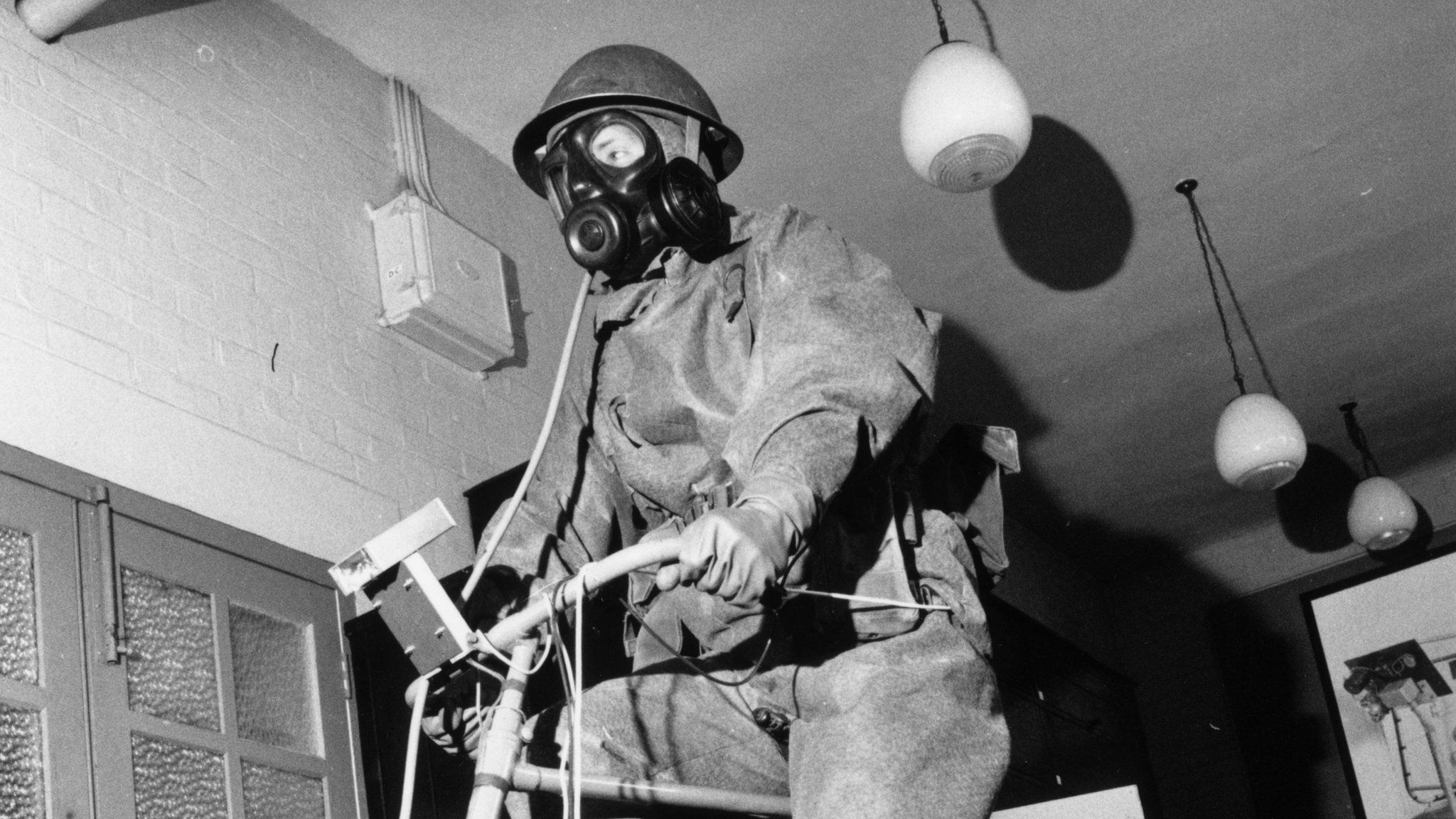 23rd May 1964: A soldier testing a respiratory mask and protective suit by pedaling on a fixed bicycle at the chemical defence establishment at Porton Down, Wiltshire