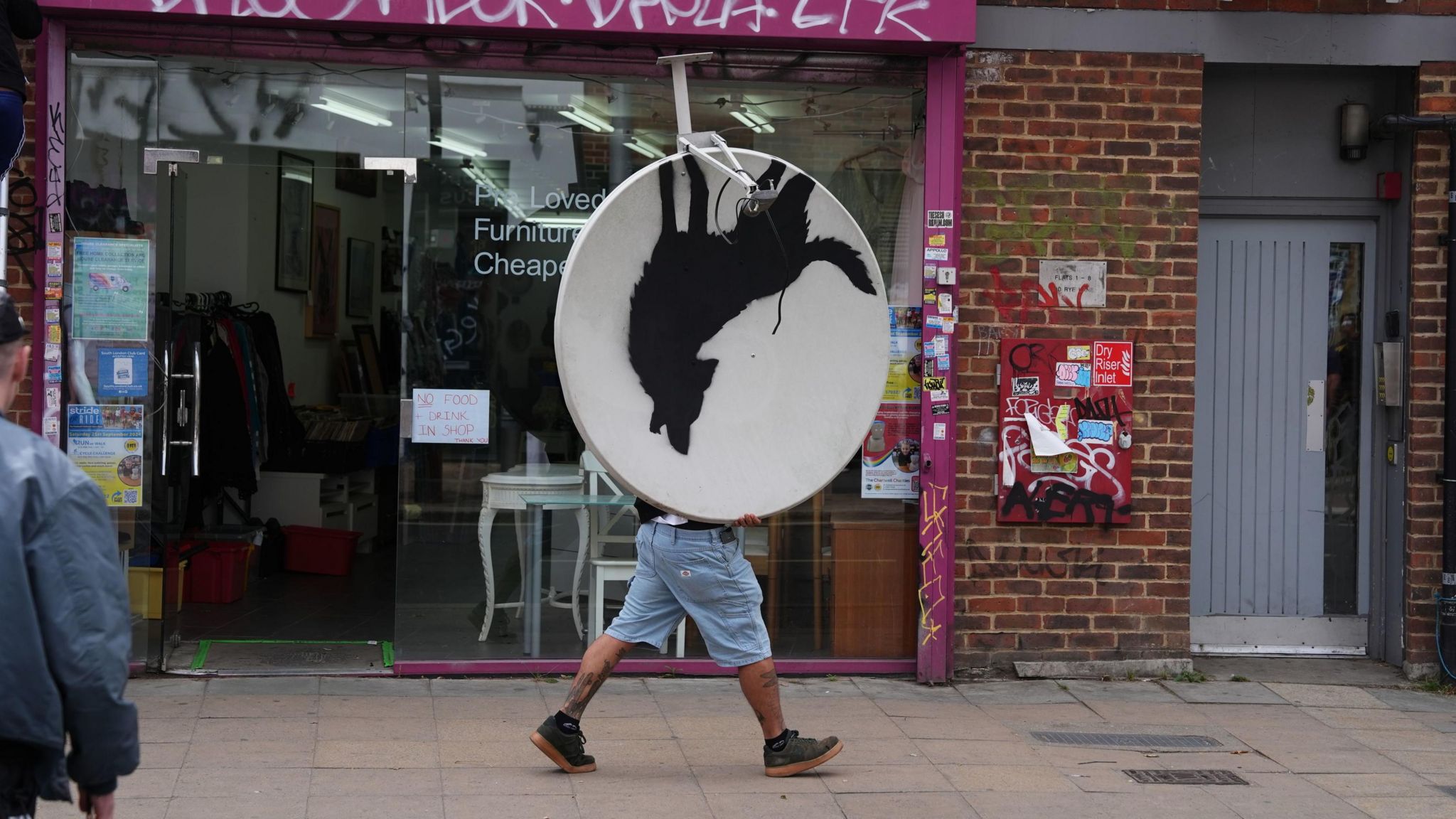 A man walks off with a satellite dish painted with the silhouette of a howling wolf