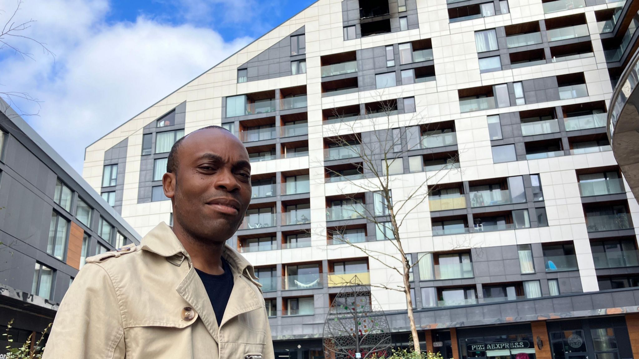 Paulin Ngon stands in front of Varney Court, a block of flats, with two balconies seen burned