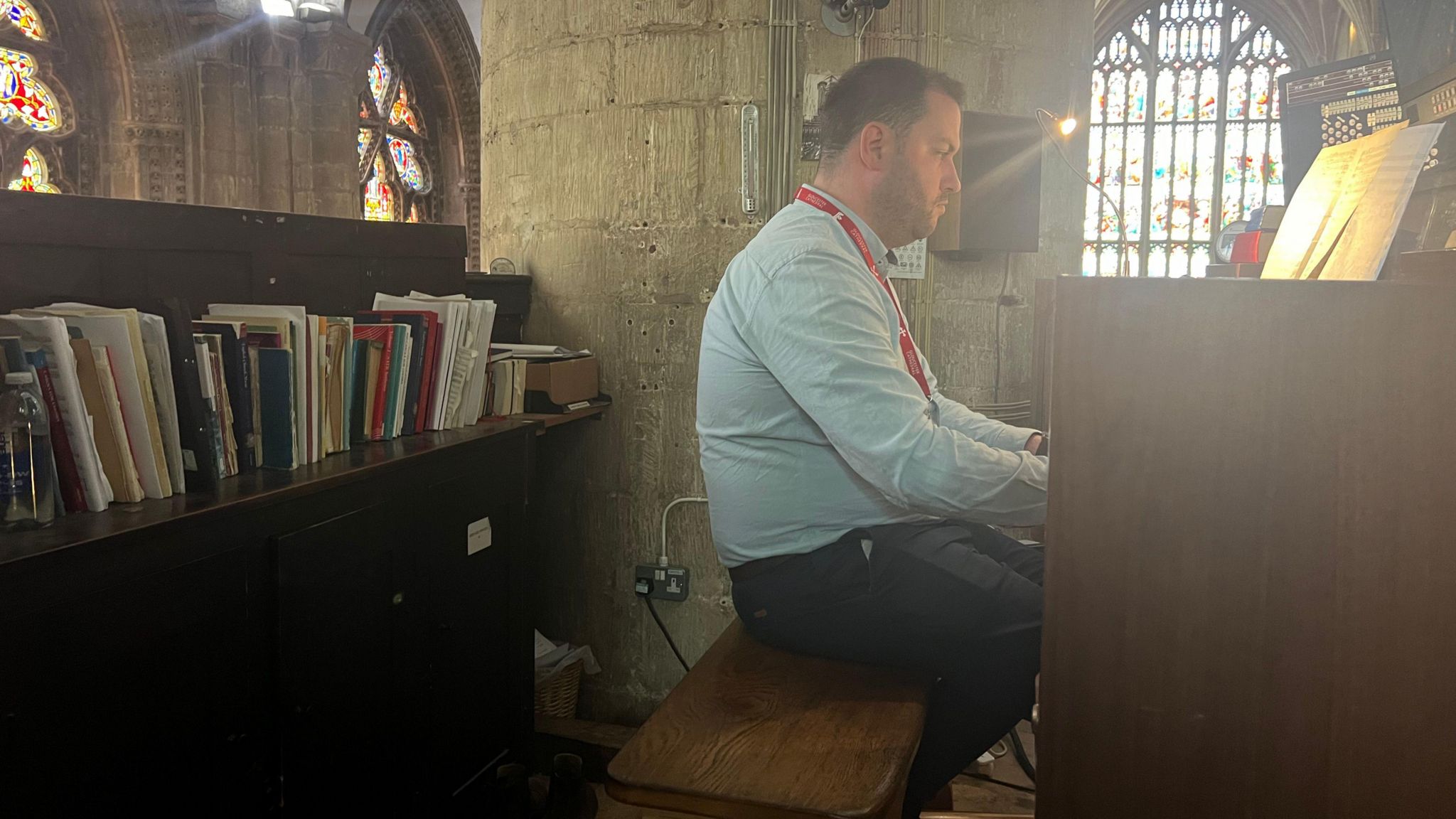 Jonathan Hope playing a digital organ at Gloucester Cathedral. He is sat next to a bookshelf.