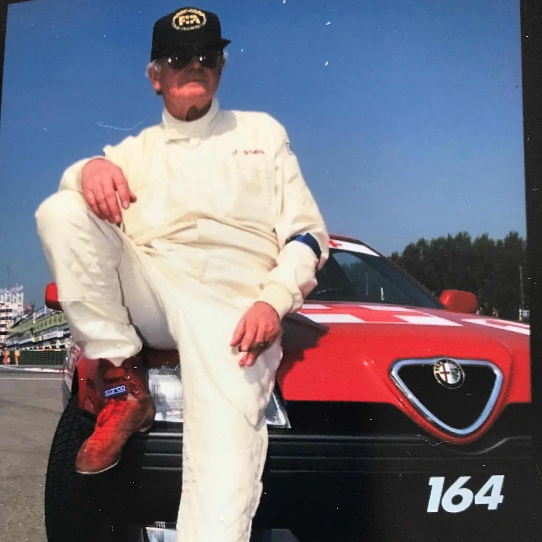 Sid Watkins sits on the bonnet of a red Alfa Romeo
